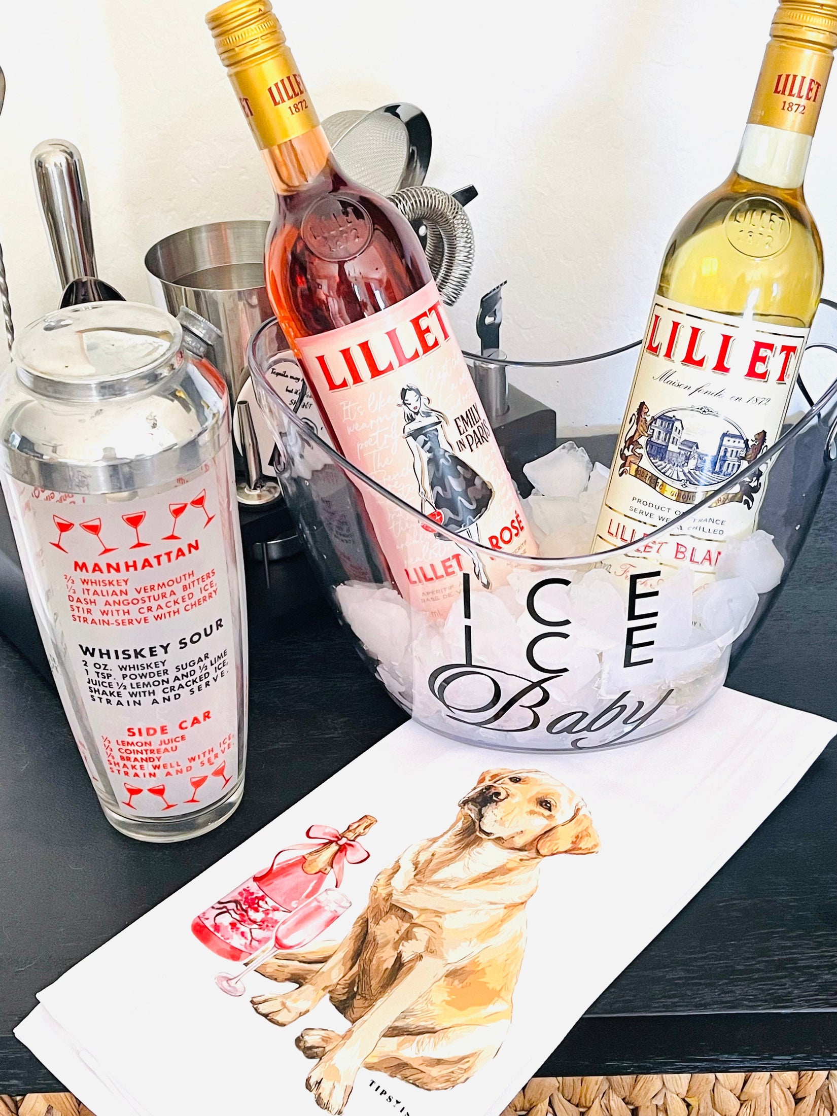 Bottles of Lillet and Manhattan cocktail mix with an ice bucket labeled 'Ice Ice Baby' on a bar counter.