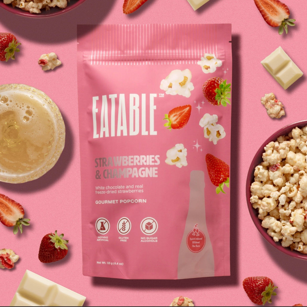 Eatable strawberries and champagne popcorn package on a pink background with strawberries, popcorn, and a drink.