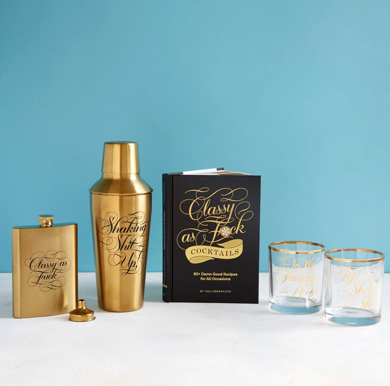 Classy as Fuck Cocktails book styled with gold cocktail shaker, flask, and rocks glasses
