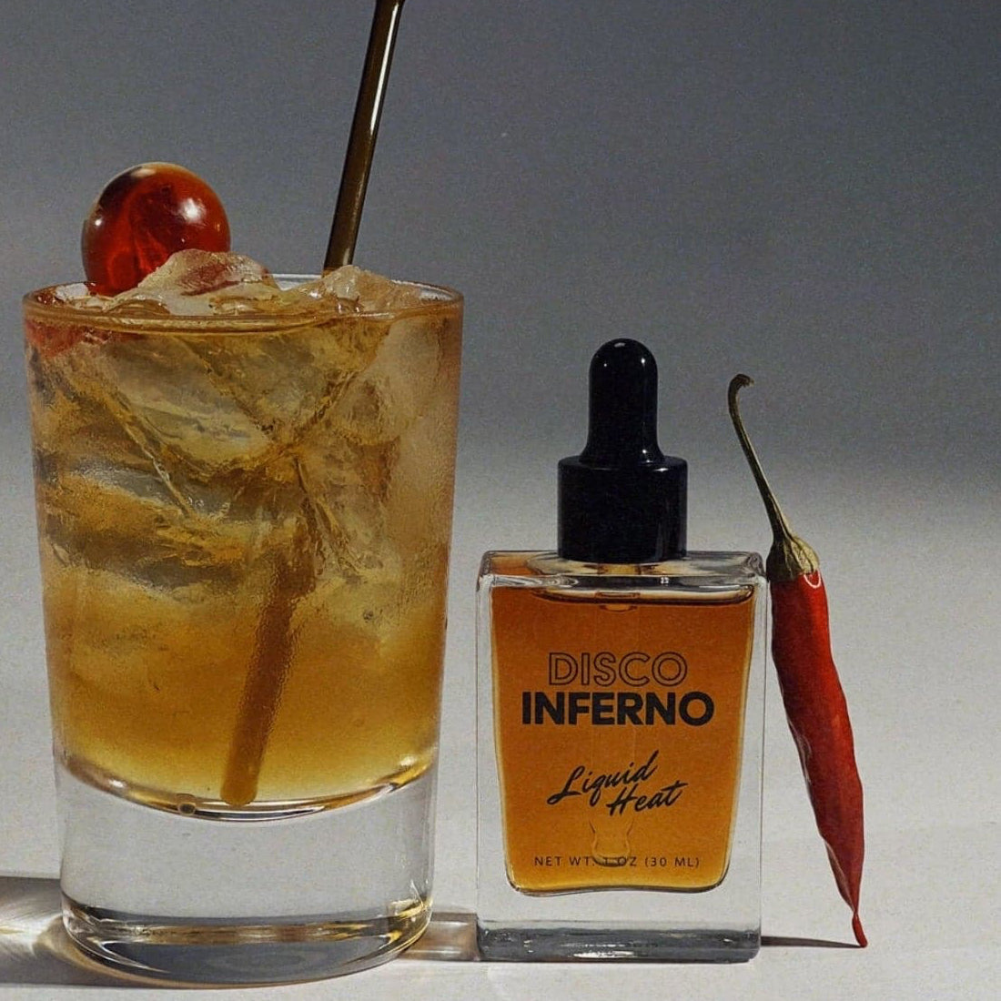 Disco Inferno: Liquid Heat Cocktail Bitters Displayed with a cocktail and red pepper