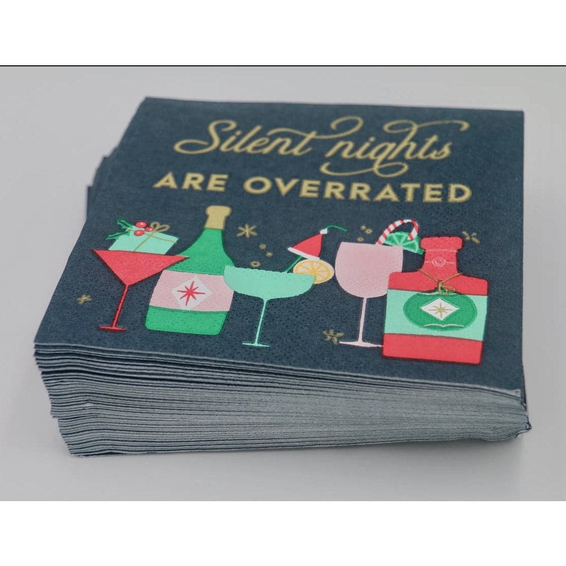 Christmas cocktail party napkins with a dark green background, differnt cocktail glassess and bottles are featured across the bottom in festive colors, and across the top in gold are the words "silent nights are overrated"