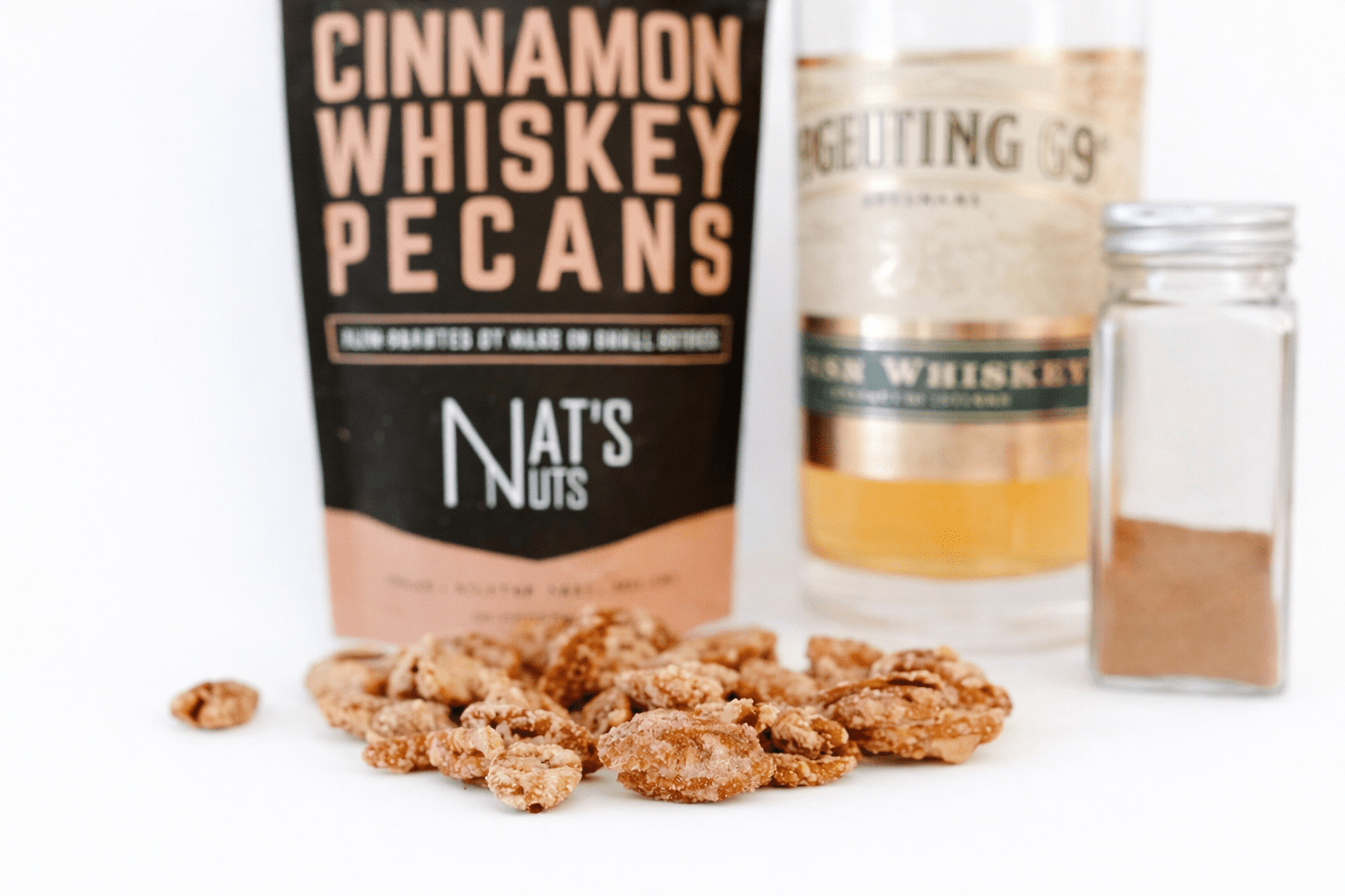 Cinnamon whiskey pecans with a bag labeled 'Nate's Nuts' and a bottle of whiskey on a white background.