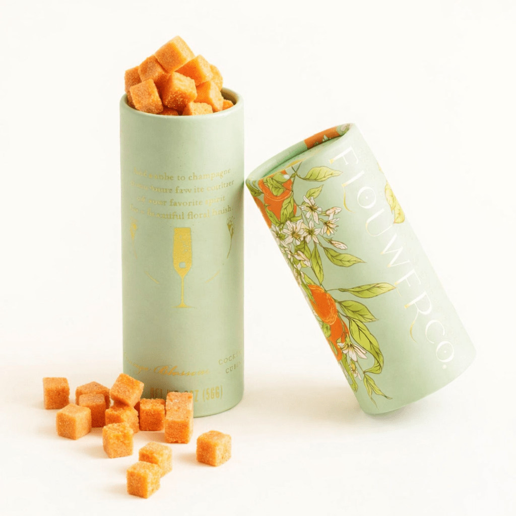 Decorative cylindrical container with floral design filled with orange cubes on a white background