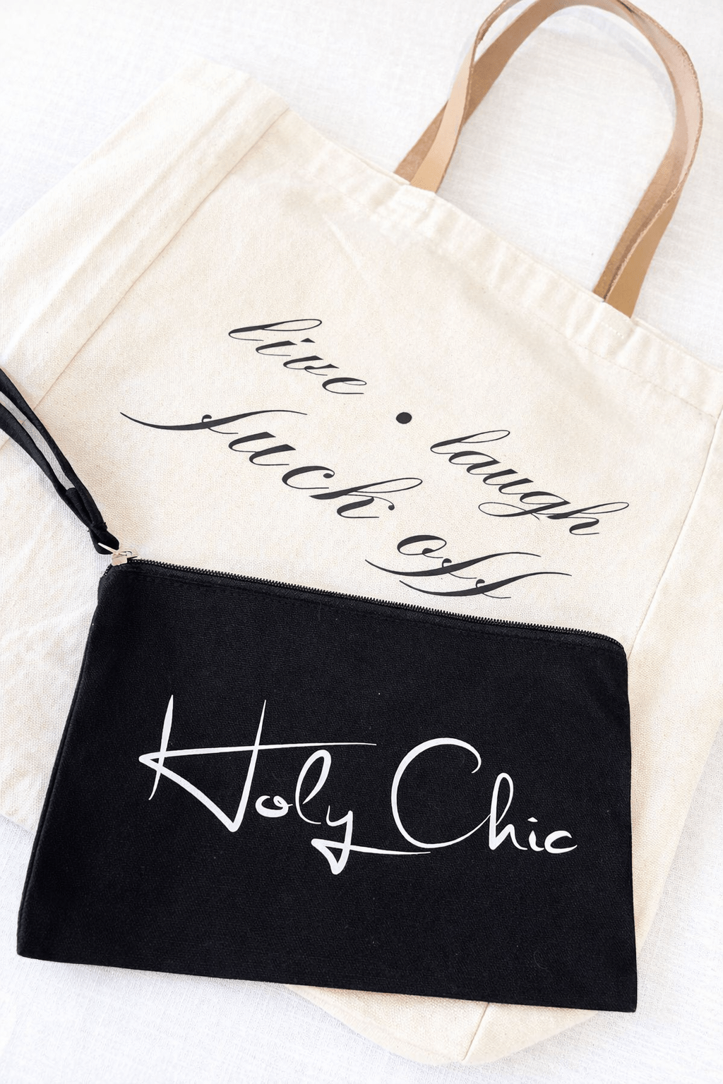 Tote bag with the words “live laugh fuck off” modeled with black wristlet that says “holy chic”