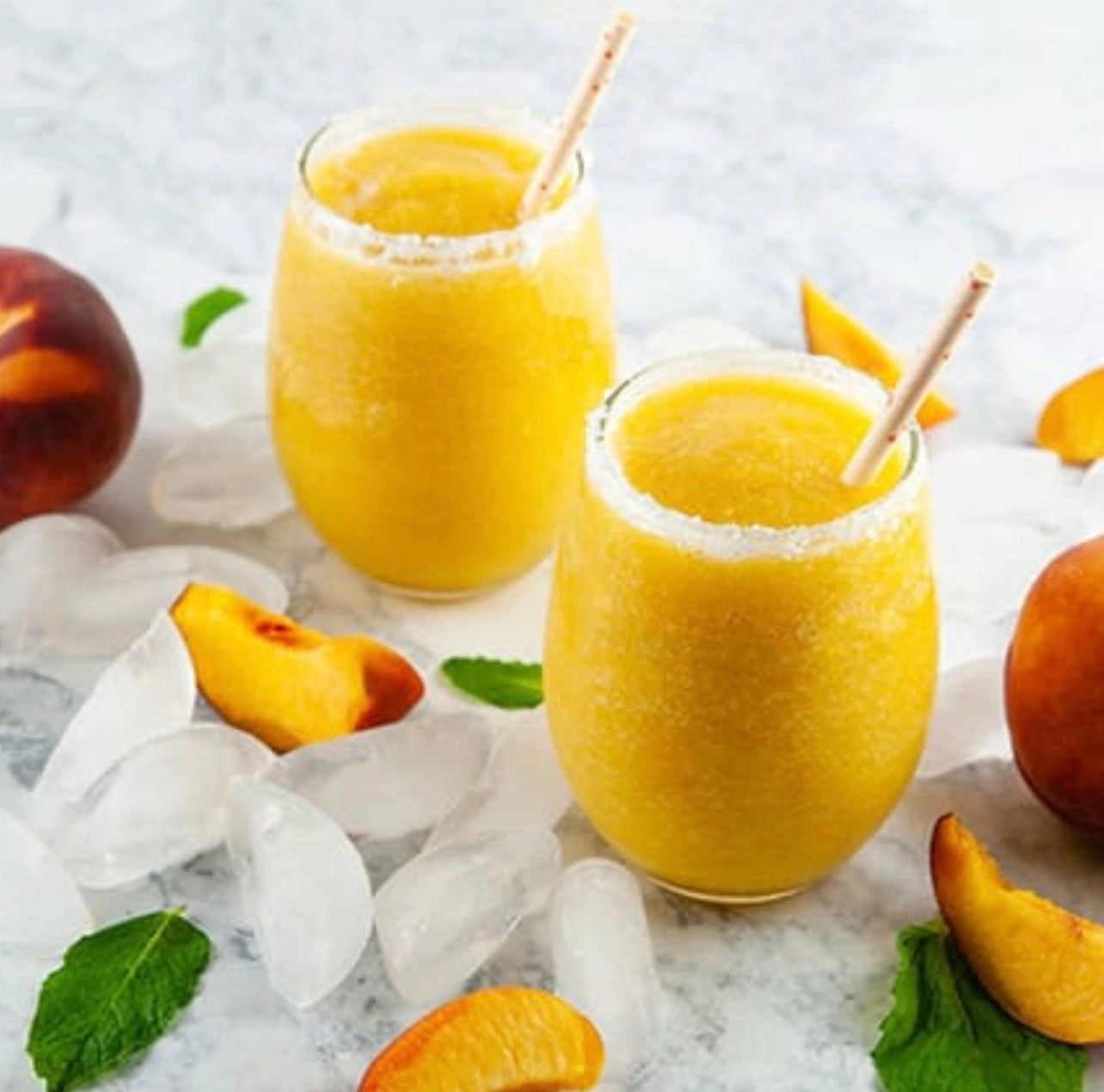 Frozen peach bellini cocktails in glasses with fresh peach garnish made using Noble Mick’s cocktail mix