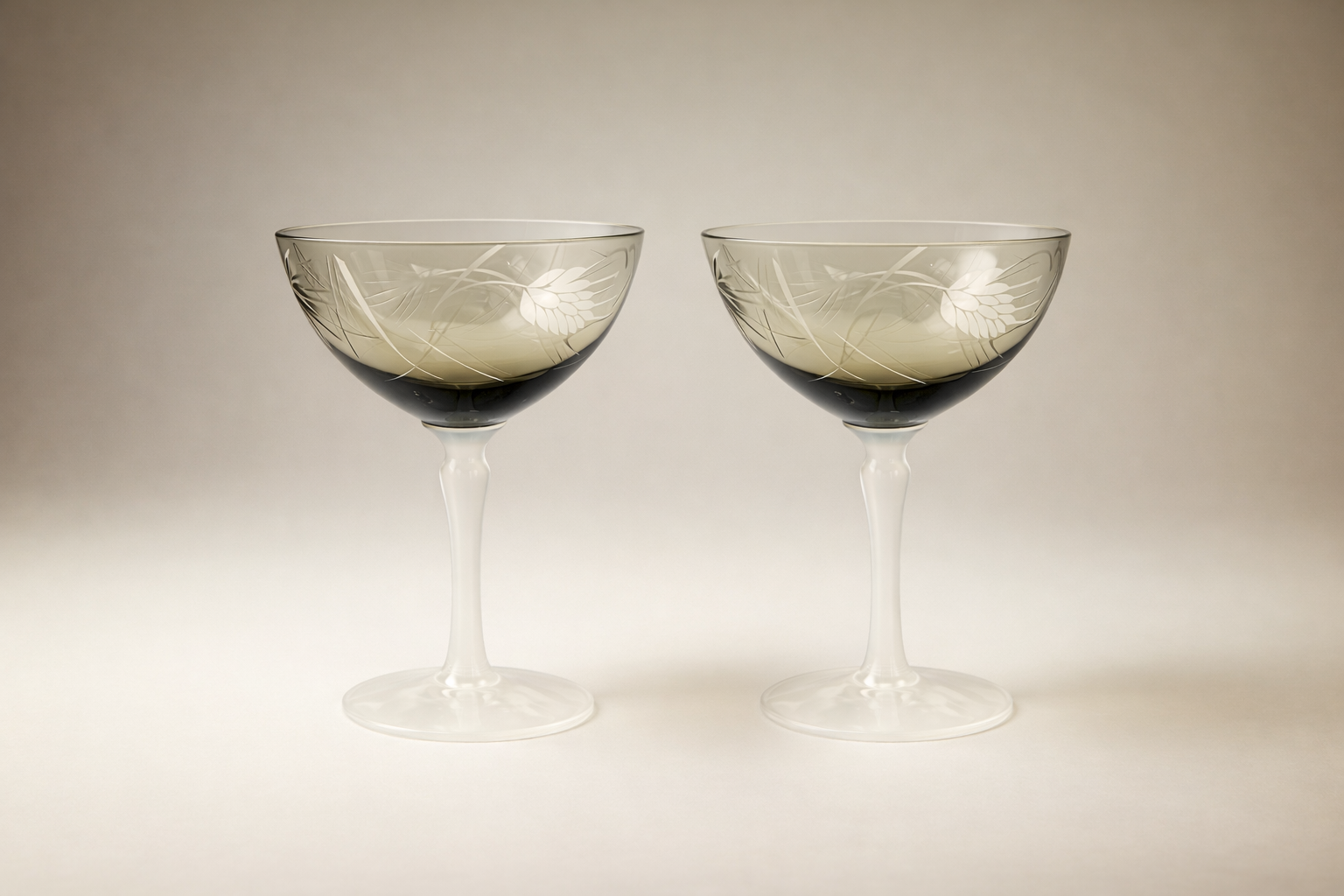 Set of two vintage coupe glasses with smoked glass bowls, white opaline stems, and etched floral design on a soft neutral background