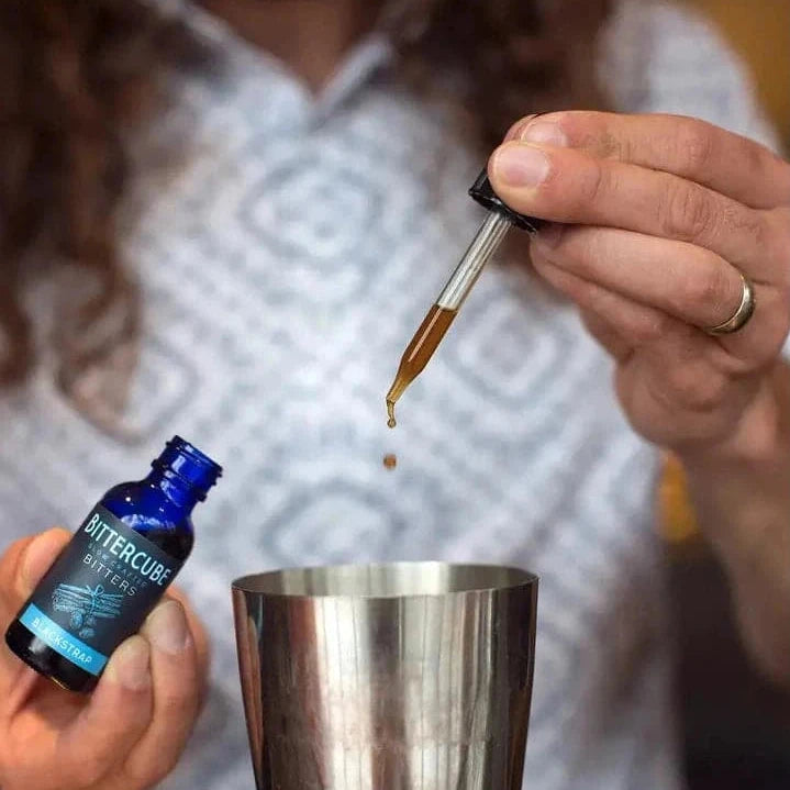 Man adding bitters to a cocktail shaker using a dropper