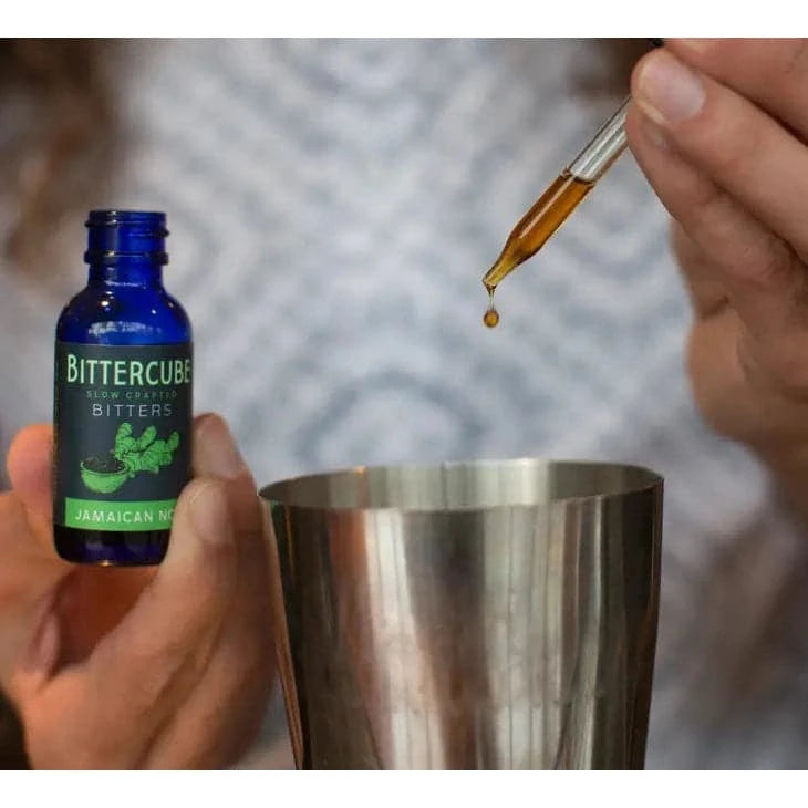 man using the dropper from the bottle of Jmaican No. 1 bitters to add the bitters into a cocktail shaker