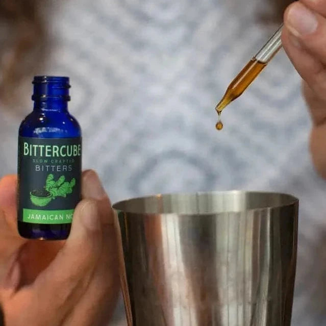 Woman using a dropper to add cocktail bitters to a cocktail shaker