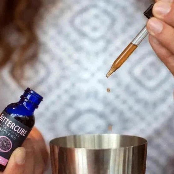 Woman using a dropper to add bitters to a cocktail shaker