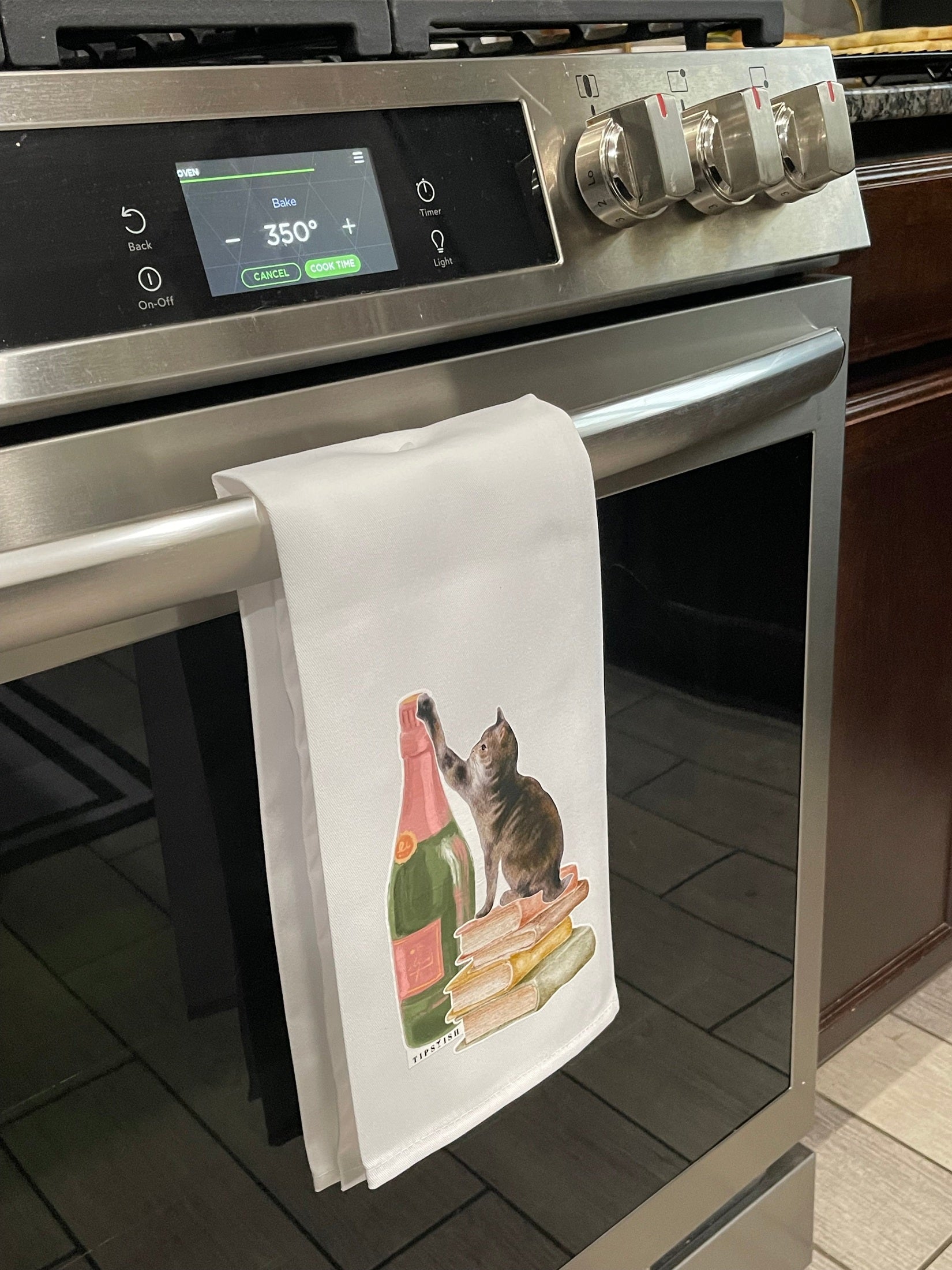 Oven with a towel featuring a cat and bottles on top