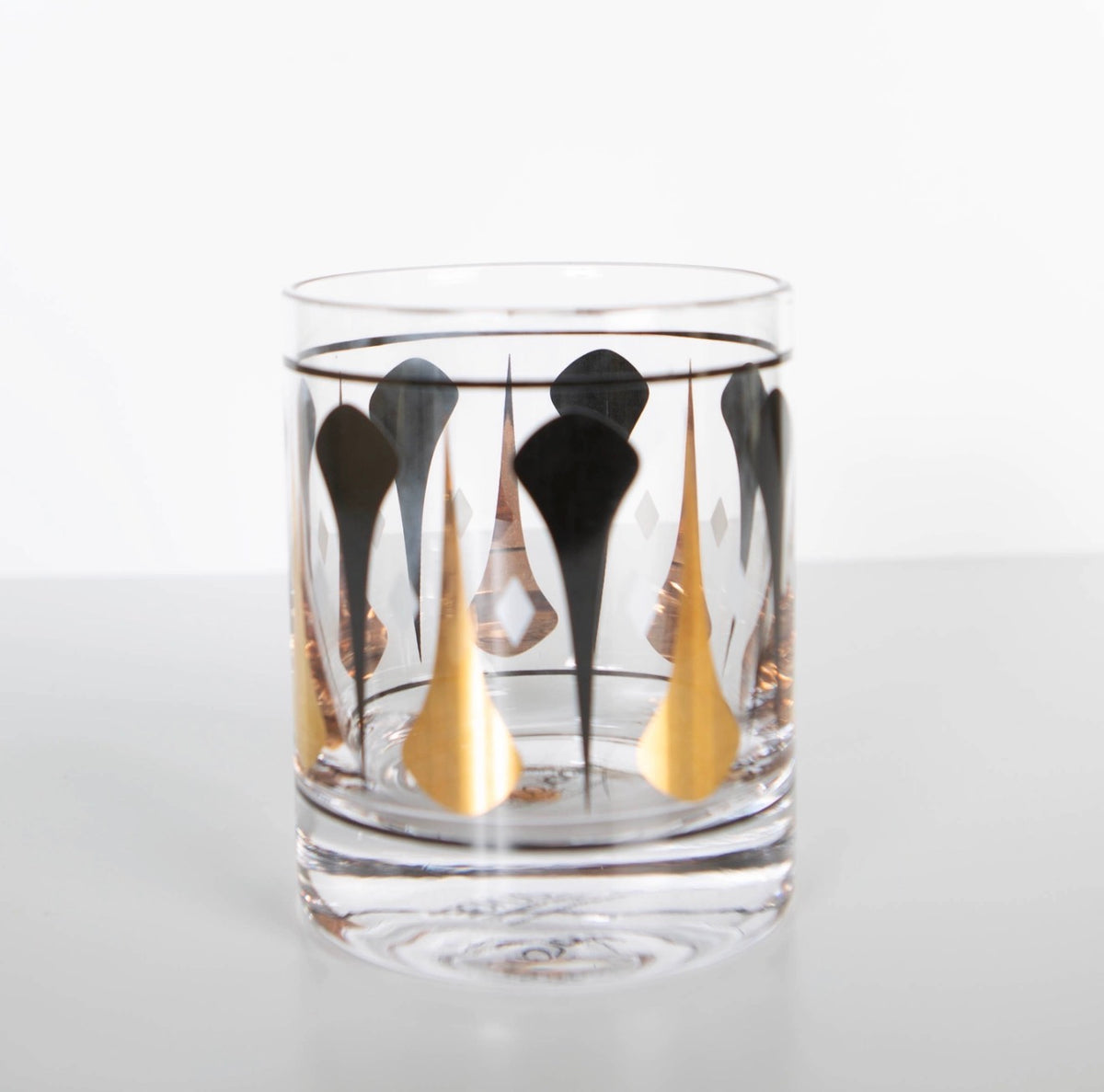 Clear 10 oz whiskey rocks glass featuring a black and metallic gold mid century dart pattern with white diamond accents