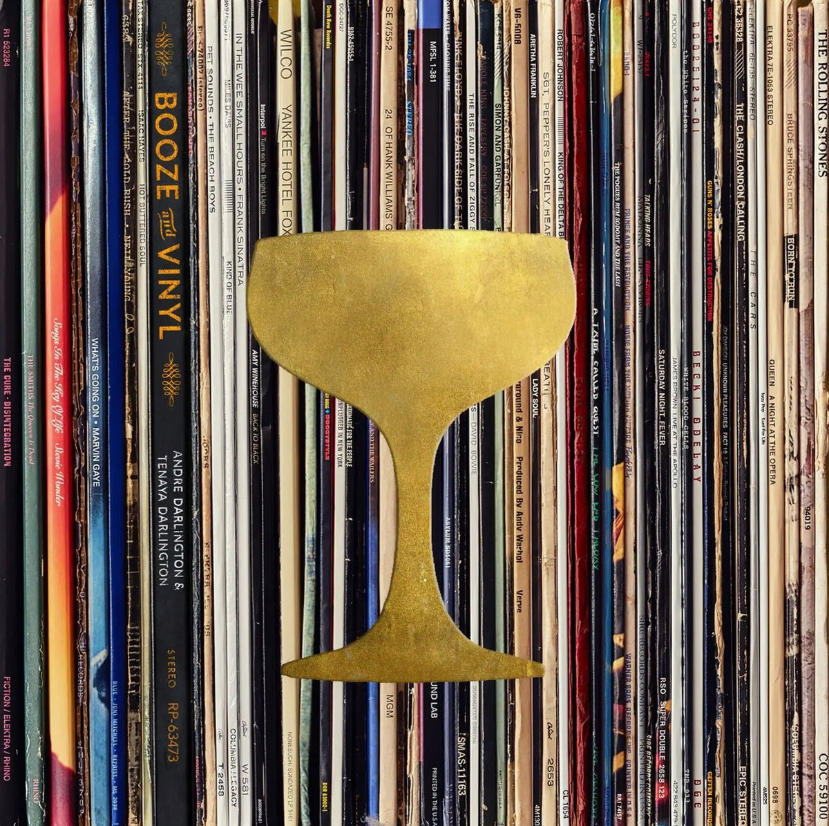 Booze & Vinyl cocktail book cover featuring a gold coupe glass silhouette against a colorful collection of vintage vinyl record sleeves.