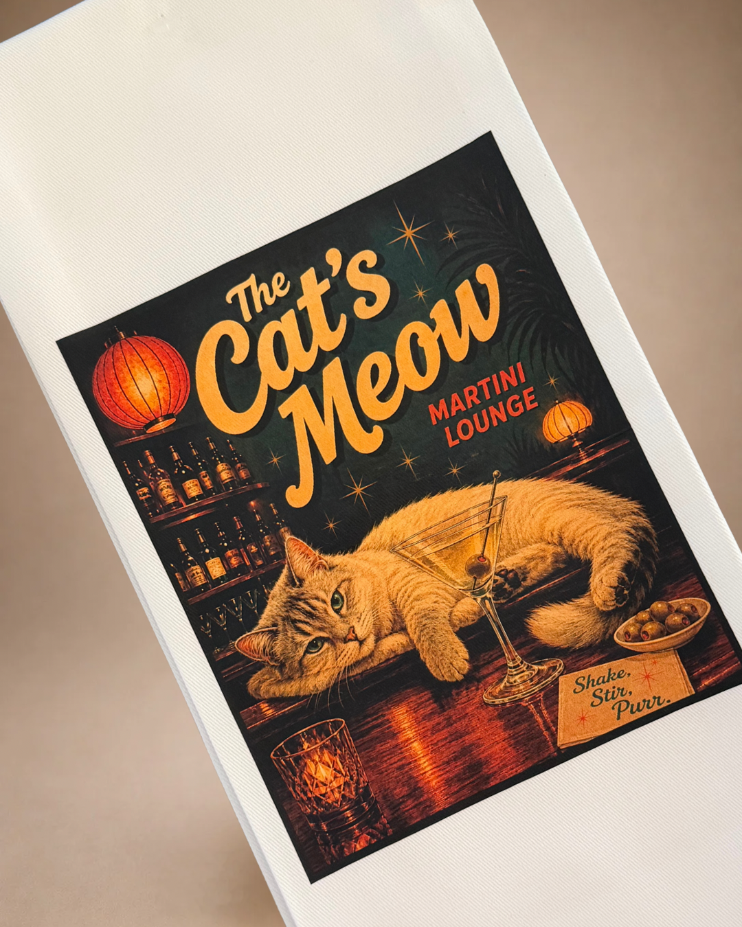 Close-up of Cat’s Meow tea towel featuring a relaxed cat at a retro cocktail bar with a martini and Shake Stir Purr design.