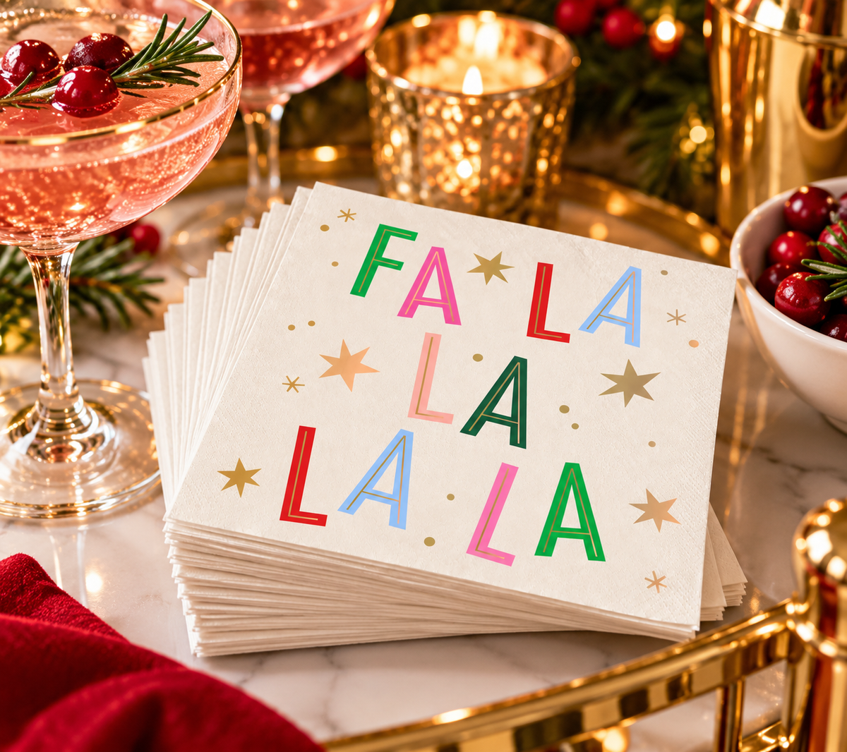 Fa La La holiday cocktail napkins styled on a festive bar with pink cocktails, cranberries, evergreen accents and gold holiday barware.