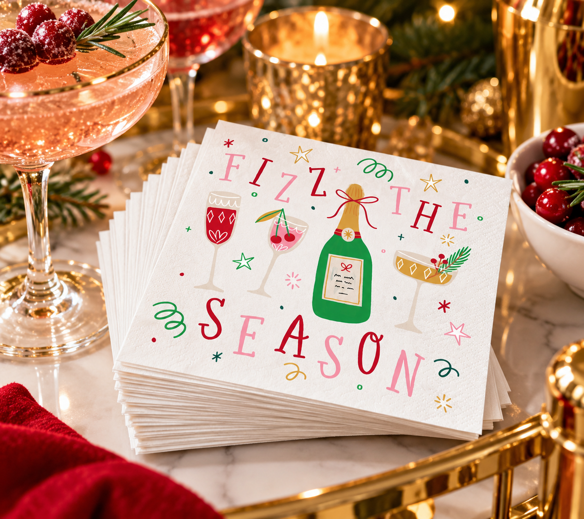 Fizz the Season holiday cocktail napkins styled on a festive Christmas bar with sparkling cocktail, cranberries, rosemary and gold holiday accents.