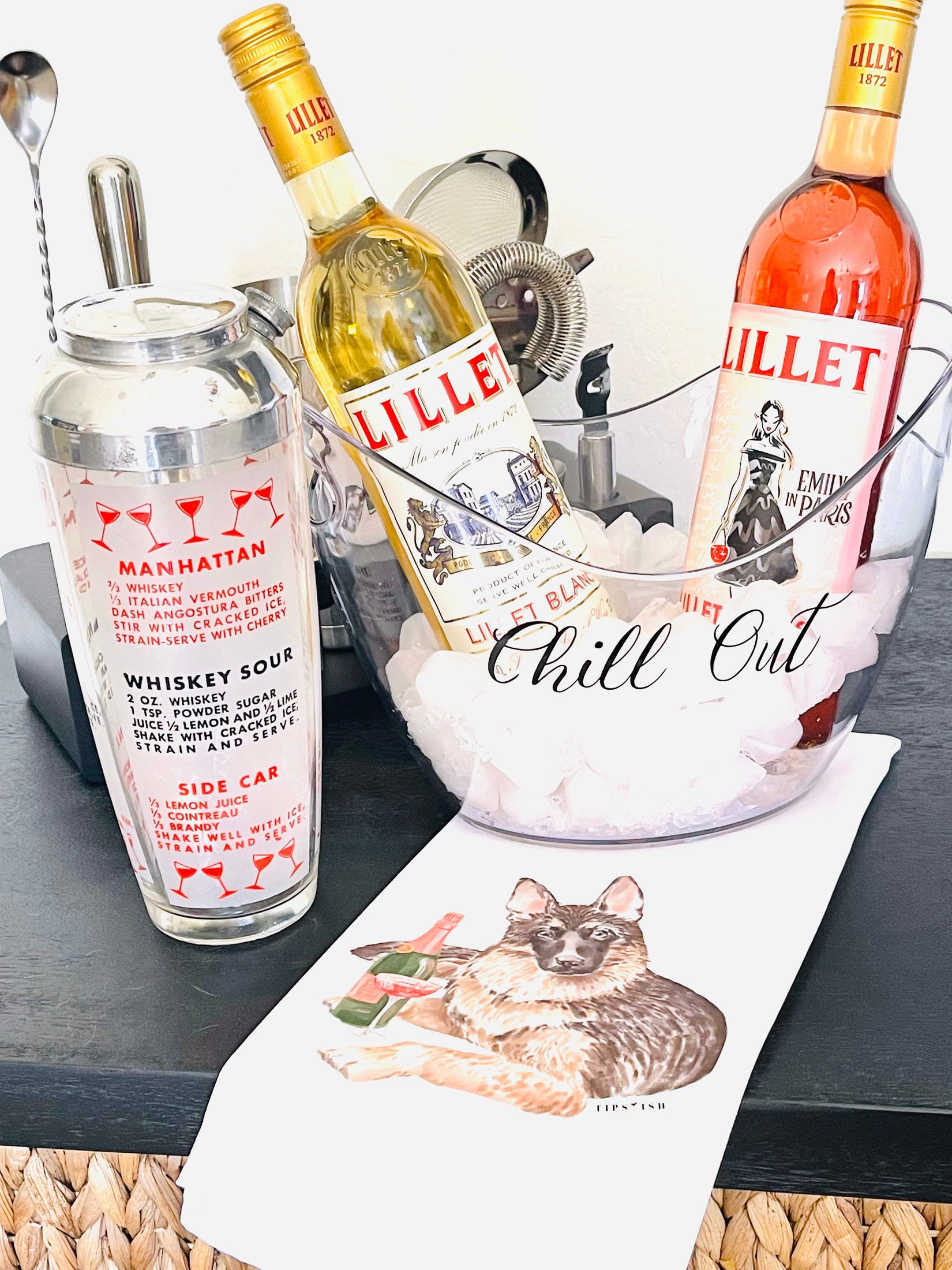 Two bottles of Lillet with a cocktail shaker and ice bucket on a table.