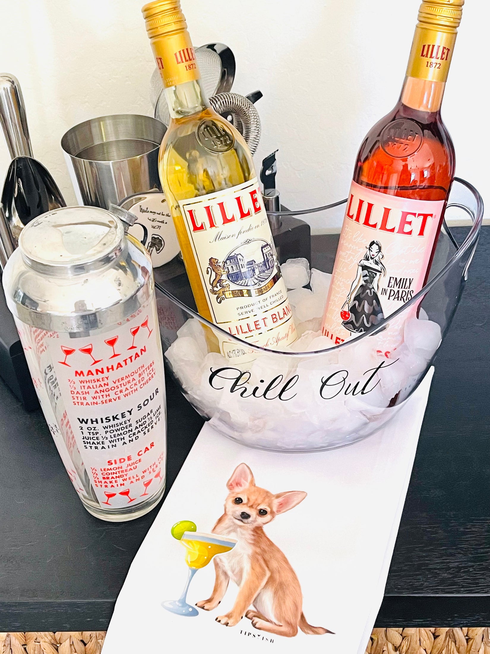 Two bottles of Lillet with a cocktail shaker and ice bucket on a bar counter.