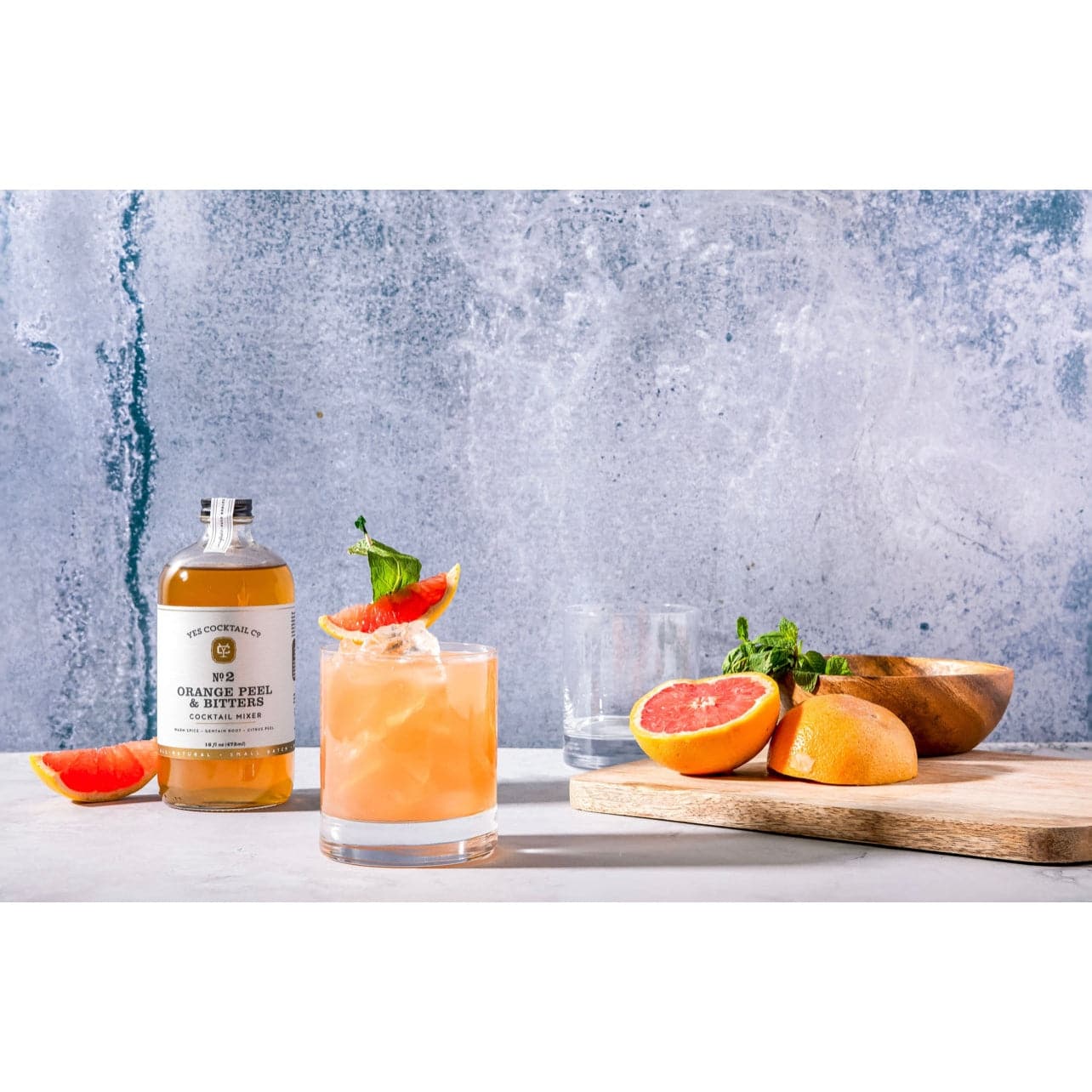 display of the Orange Peel and Bitters Cocktail Mixer on a marble countertop surrounded by fresh citrus and a finished cocktail in a double old fashioned glass