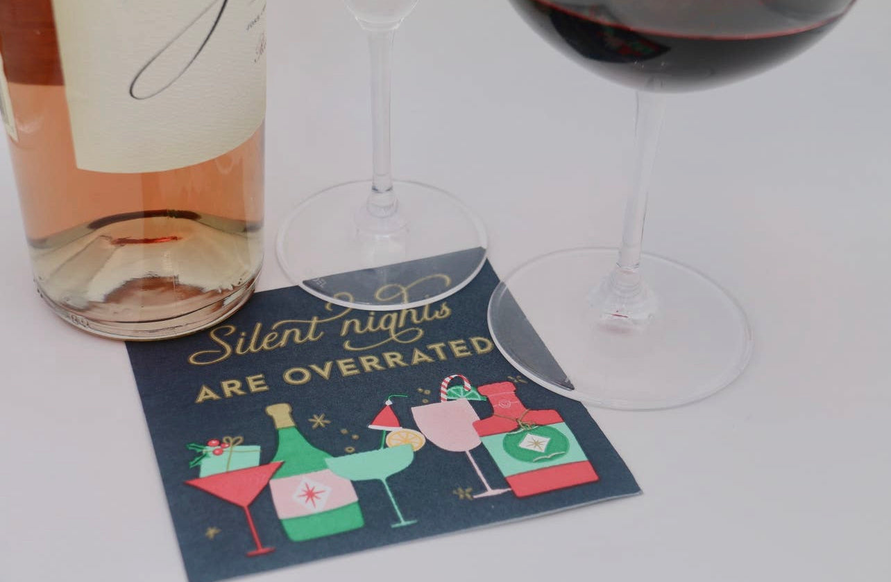 Christmas cocktail party napkins with a dark green background, differnt cocktail glassess and bottles are featured across the bottom in festive colors, and across the top in gold are the words "silent nights are overrated" displayed with a wine bottle and wine glasses