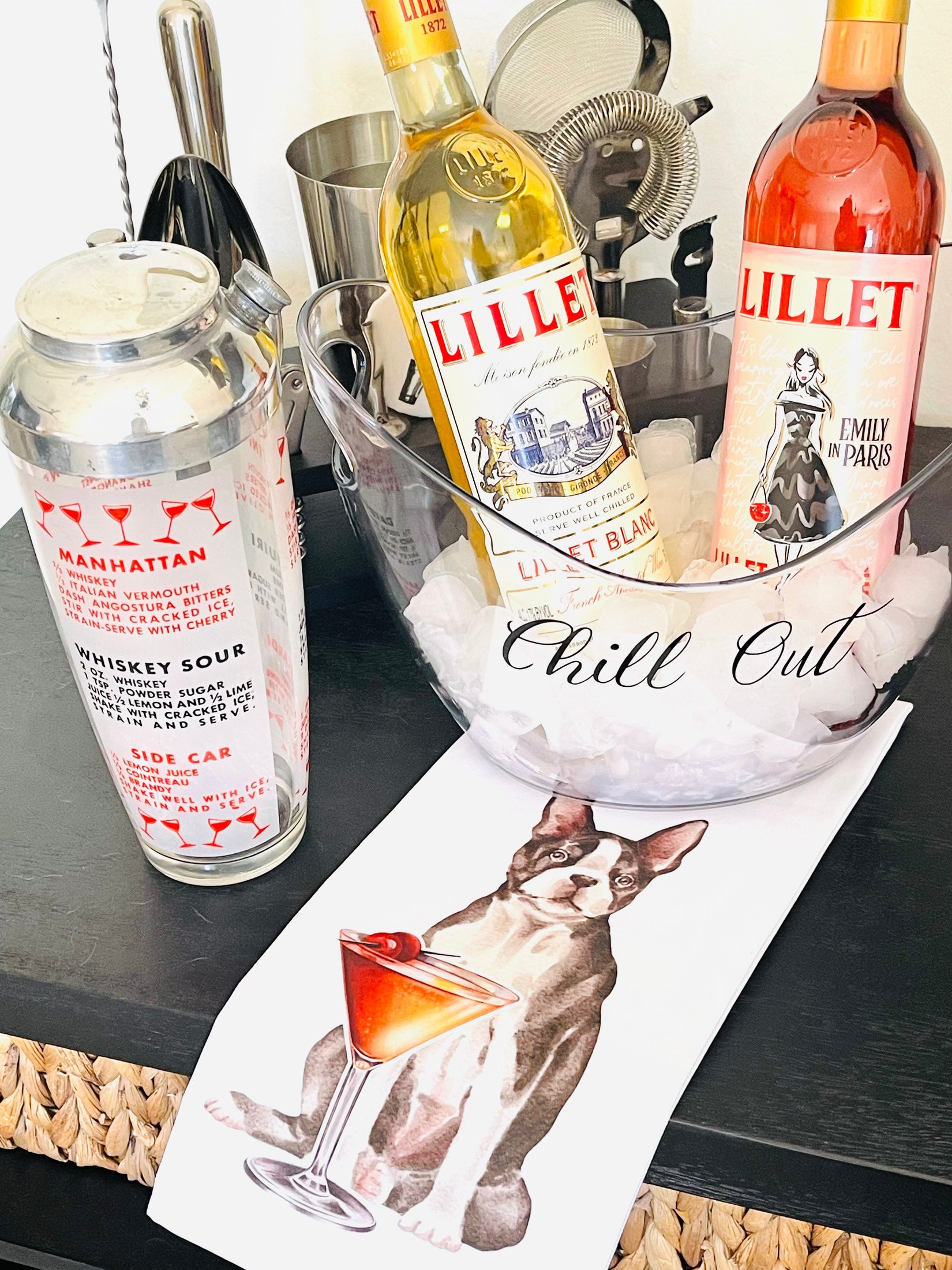 Two bottles of Lillet wine on a bar counter with a cocktail shaker and a magazine featuring a dog and a cocktail.
