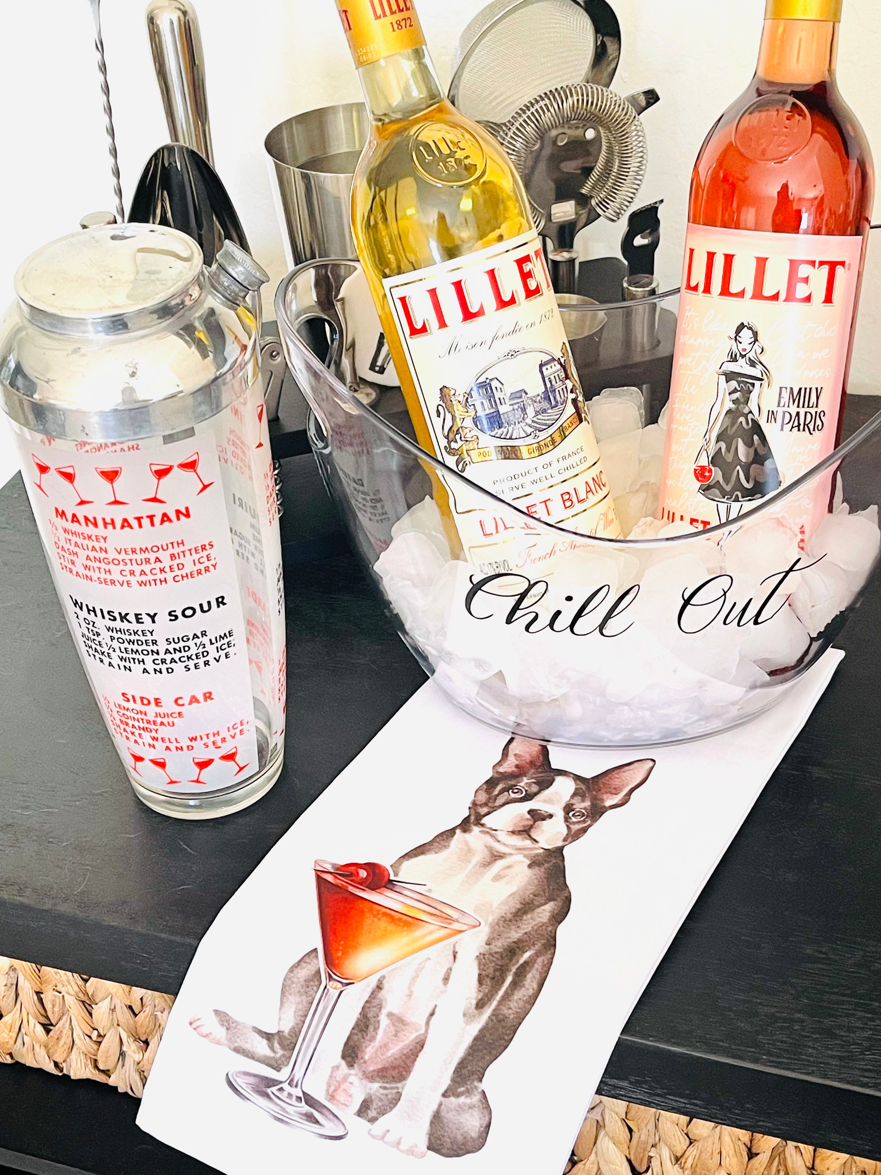 Two bottles of Lillet wine on a bar counter with a cocktail shaker and a magazine featuring a dog and a cocktail.