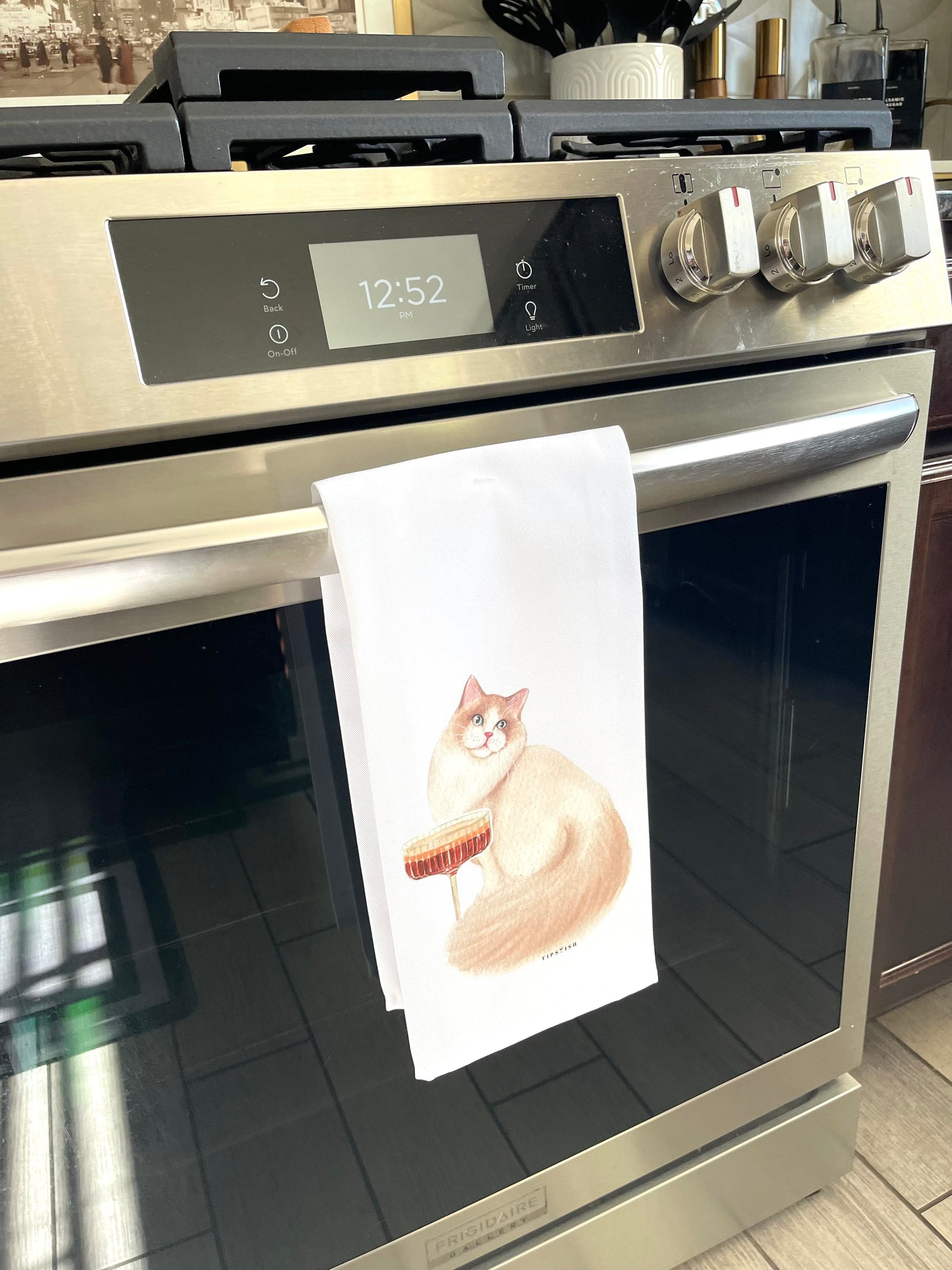 Stainless steel oven with a towel featuring a cat design hanging on the handle.