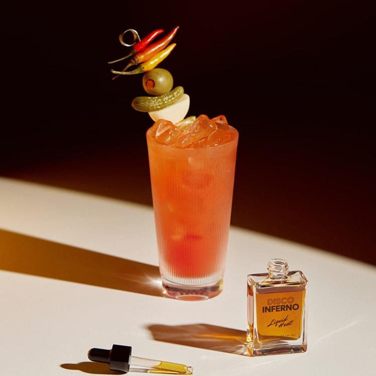 Disco Inferno: Liquid Heat Cocktail Bitters Displayed with a cocktail garnished with olives and peppers
