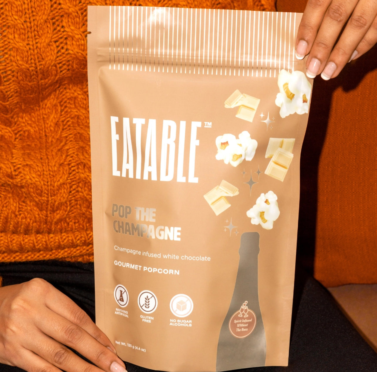 Eatable gourmet popcorn package held by a person against an orange background