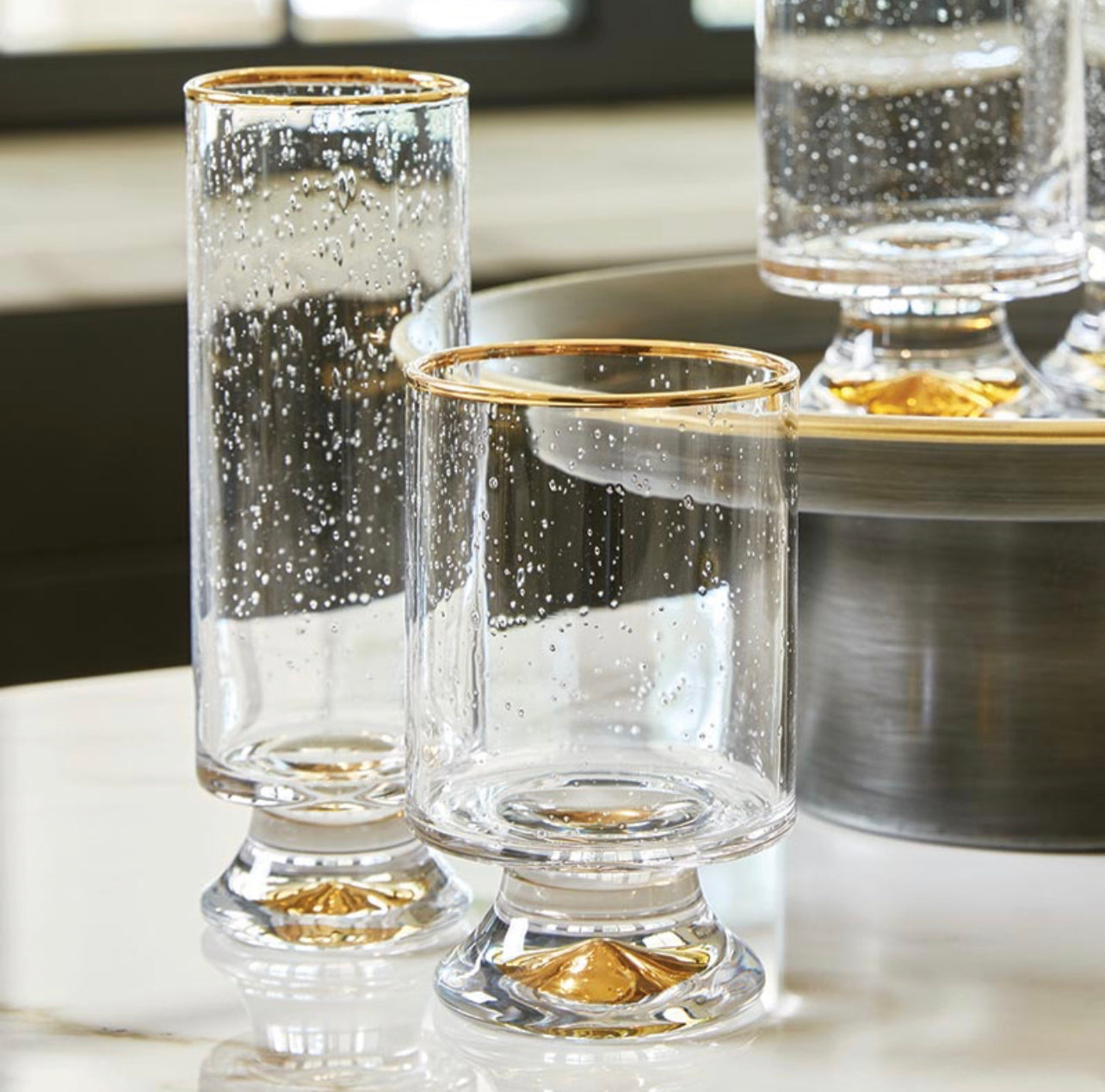 display of double old fashioned glass with matching champagne glass, both featuring clear seeded glass and gold rims