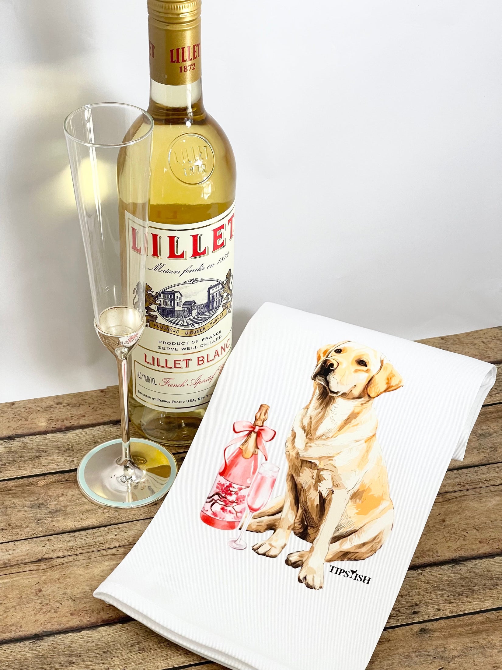 Bottle of Lillet Blanc with a glass and a tea towel featuring a dog on a wooden surface.