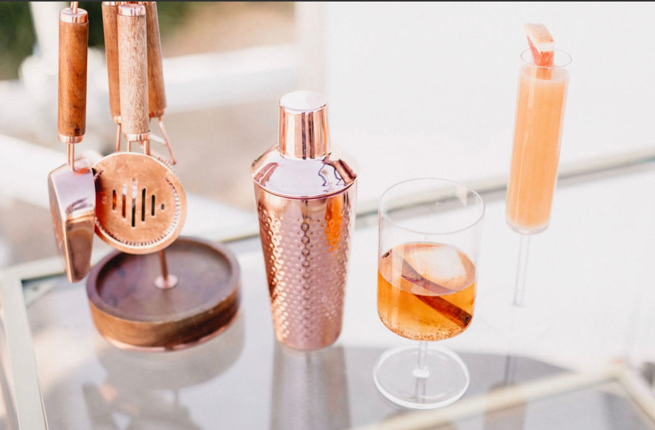 champagne and cocktail glass displaying cocktails made with the Orange Peel and Bitters mix with copper bar tools and shaker as accents