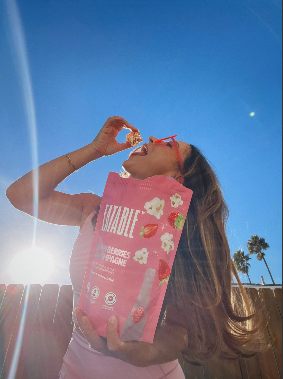 Woman eating popcorn from a bag labeled 'Gâteable' against a blue sky.