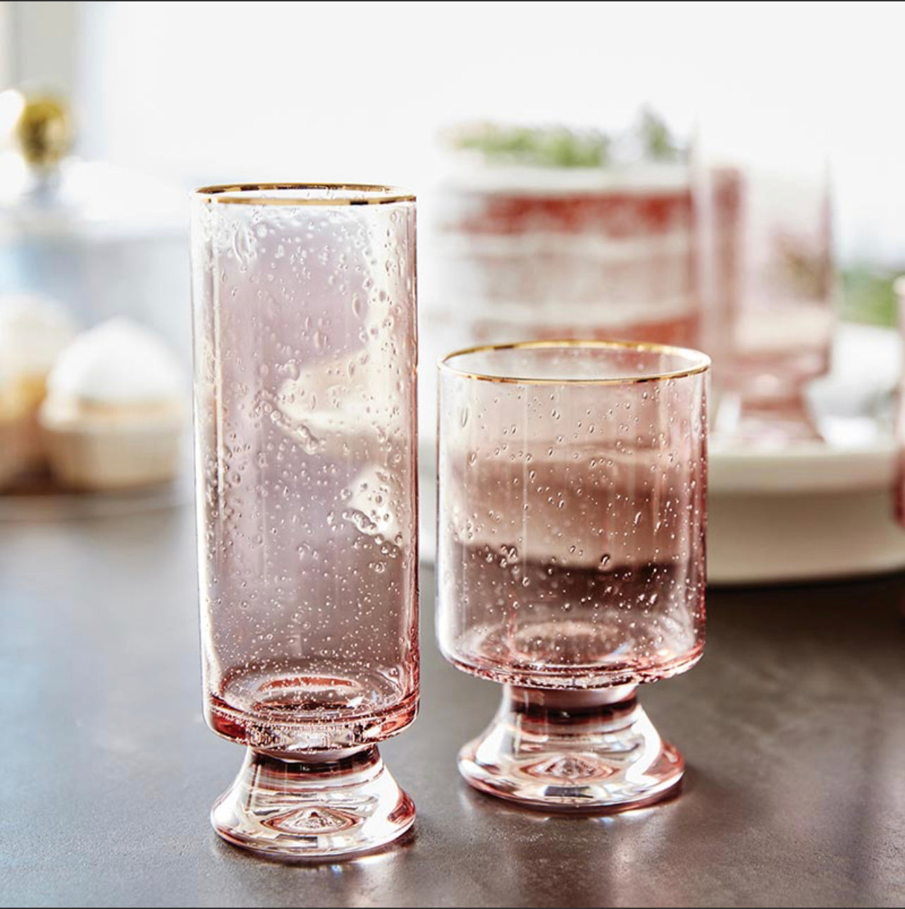 double old fashioned glass with matching champagne glass featuring seeded glass in a blush pink and hand painted gold rims on a table decorated for the holidays