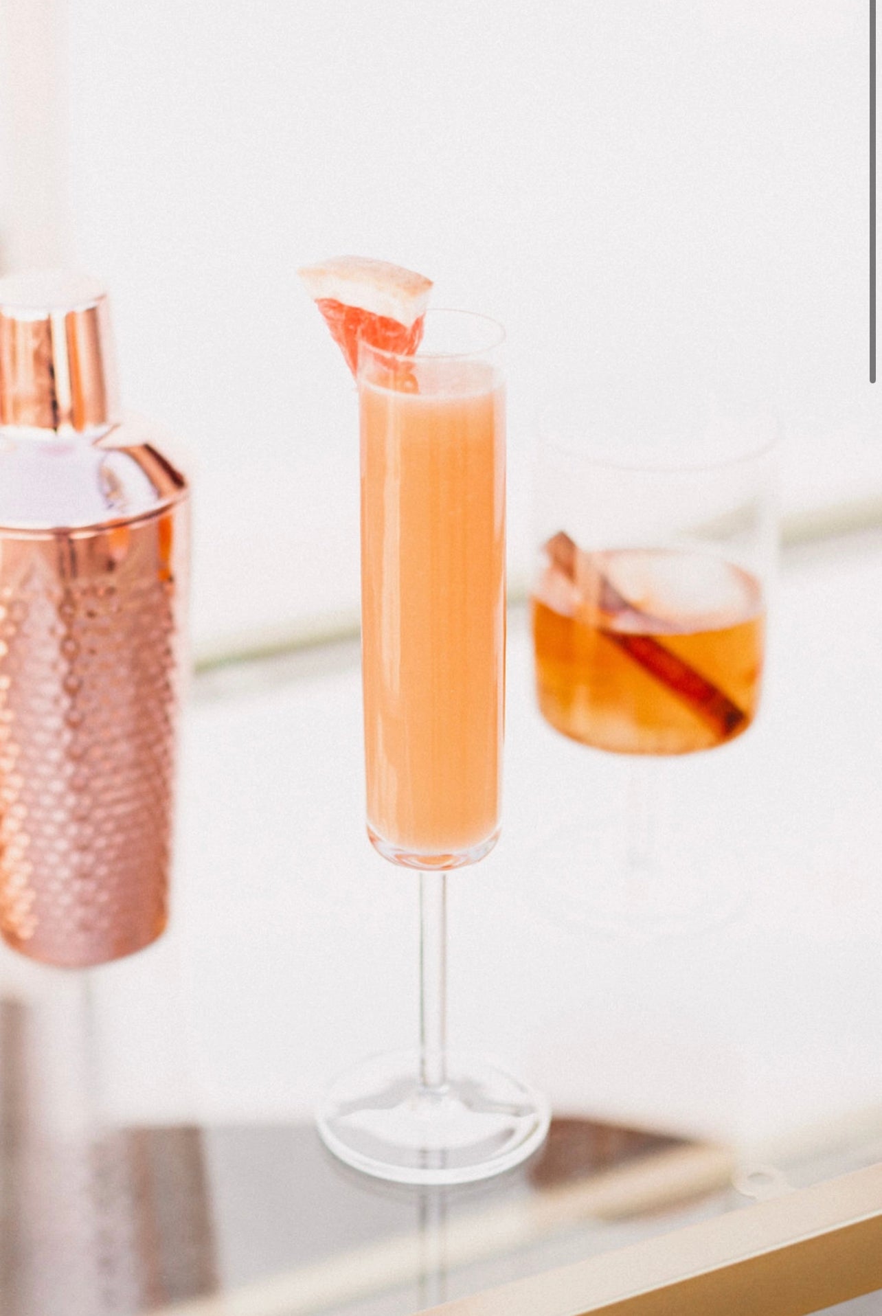champagne glass and clear stemmed cocktail glass displaying a cocktail made with the Orange Peel and Bitters Mix garnished with a cinnamon stick