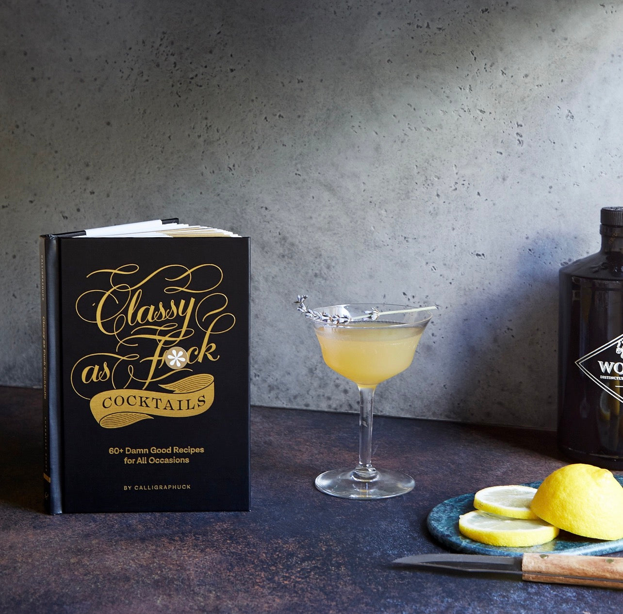 Cocktail book displayed next to a freshly made yellow cocktail and sliced lemons