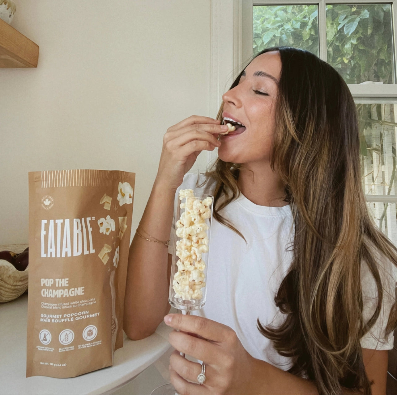 Woman eating popcorn from a clear container next to a bag of Eatable popcorn.