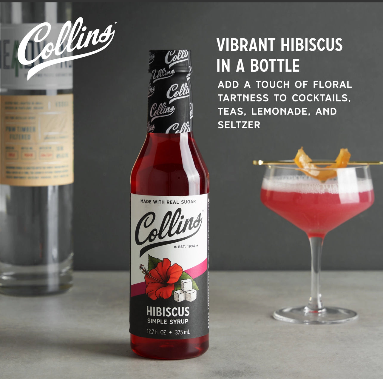 Collins Hibiscus Simple Syrup bottle with a cocktail in the background