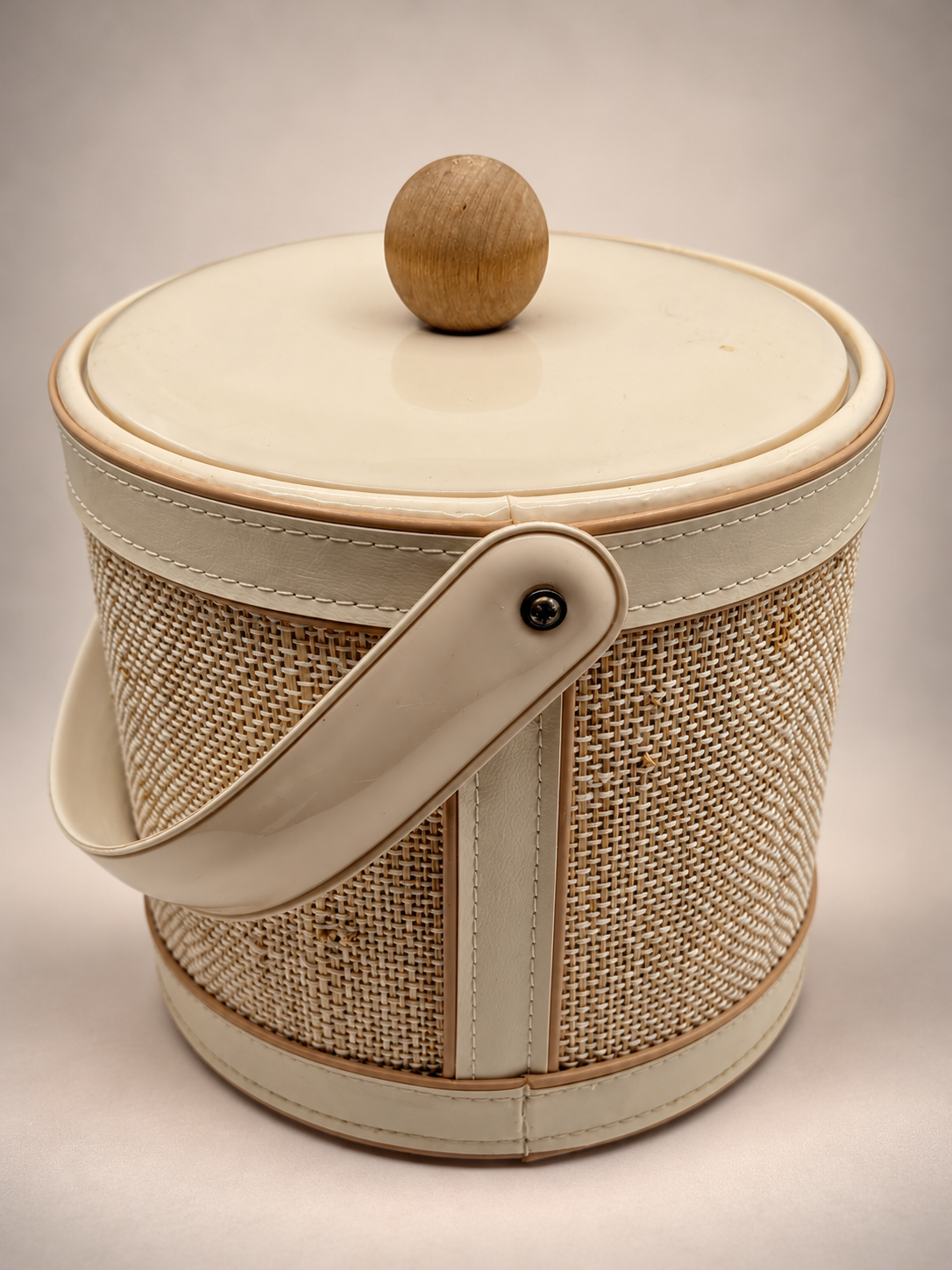 Side view of vintage Georges Briard ice bucket showing textured woven exterior, stitched ivory trim and swing handle.