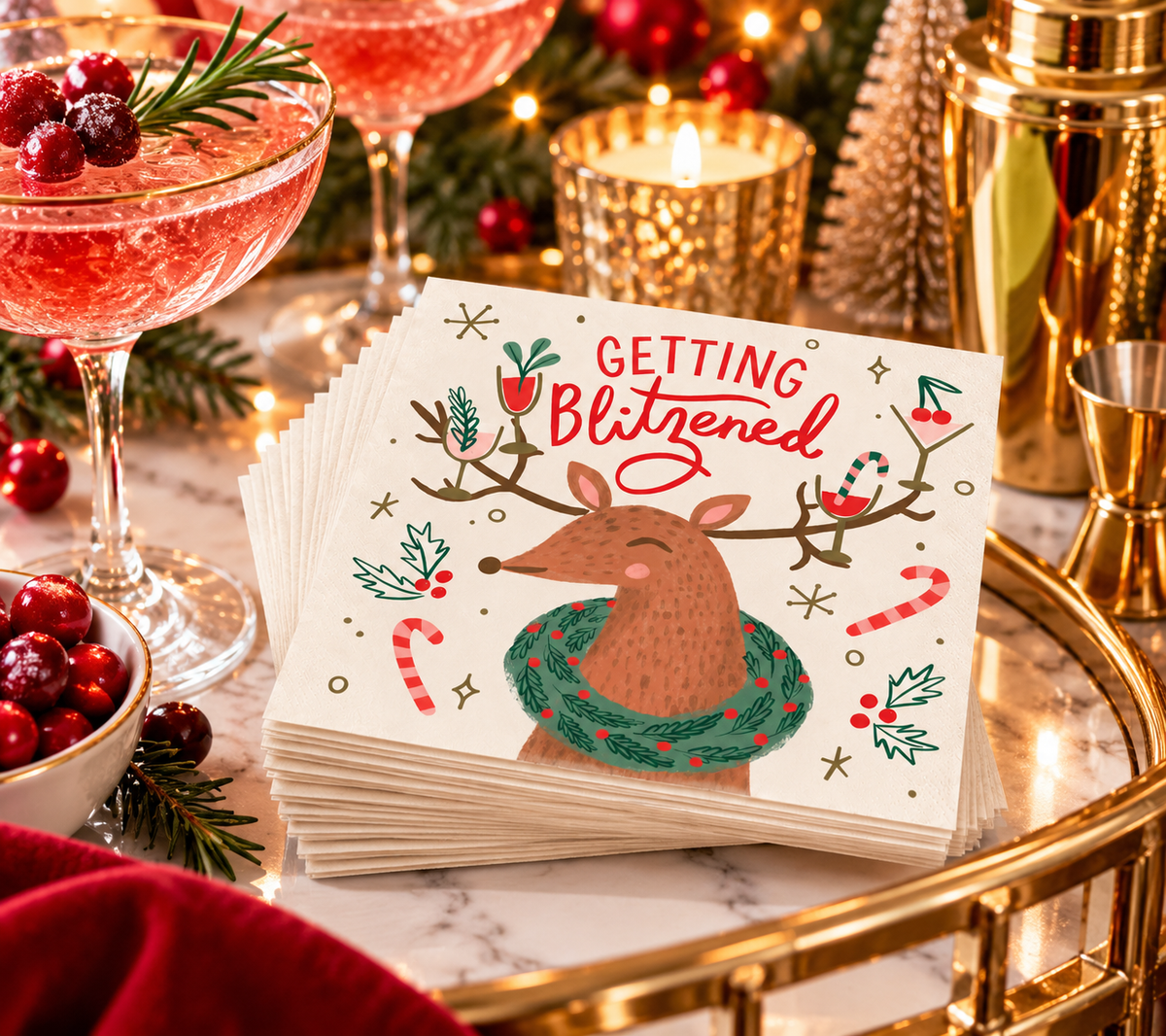 Getting Blitzened holiday cocktail napkins styled on a festive bar cart with pink cocktails, cranberries, greenery and gold barware.