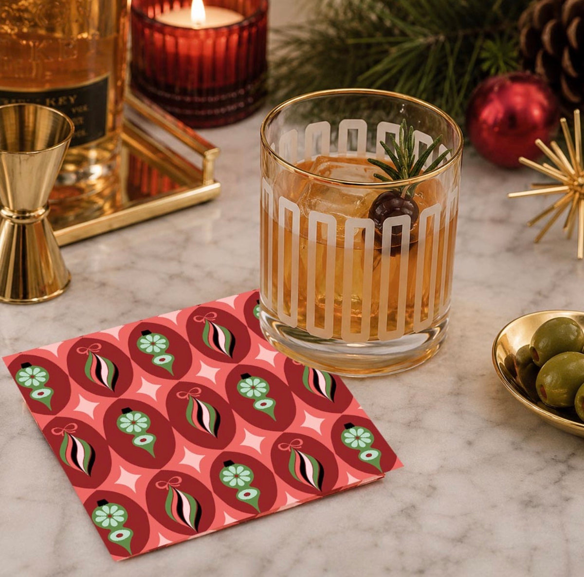 Frosted geometric gold rim cocktail glass styled with whiskey, rosemary and cherry in a festive retro bar setting