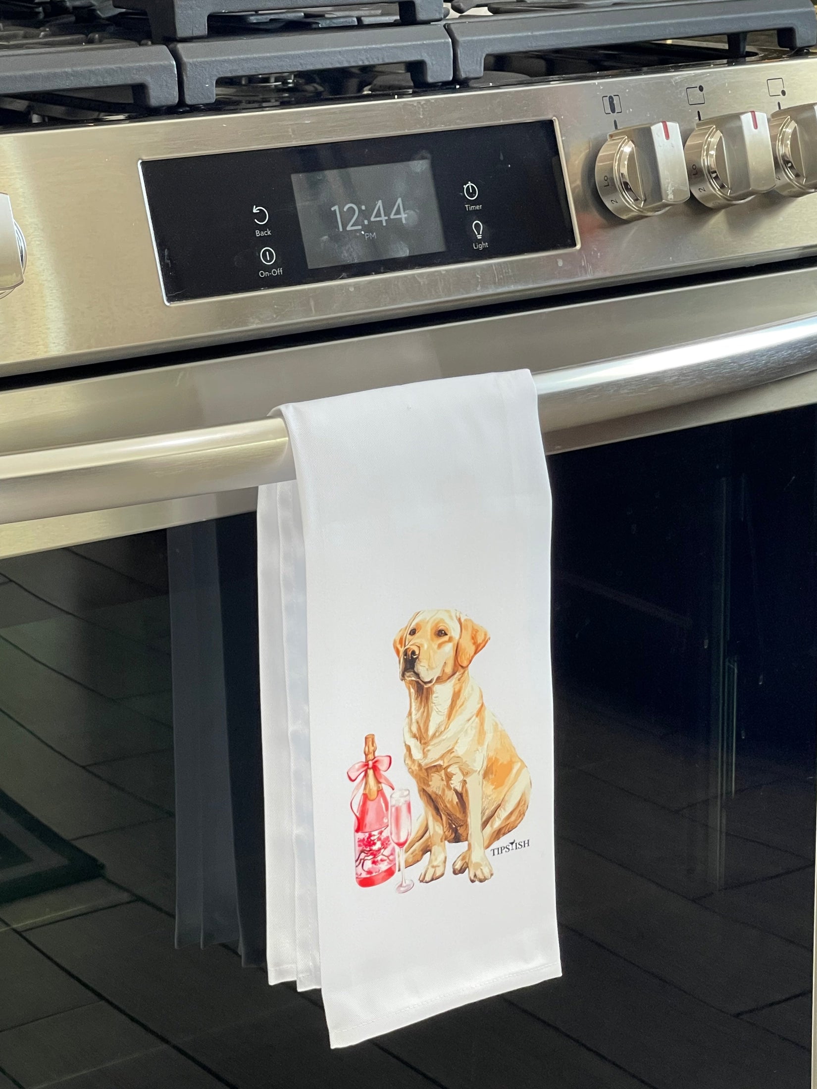 Tea towel with a dog design hanging on a kitchen oven handle.