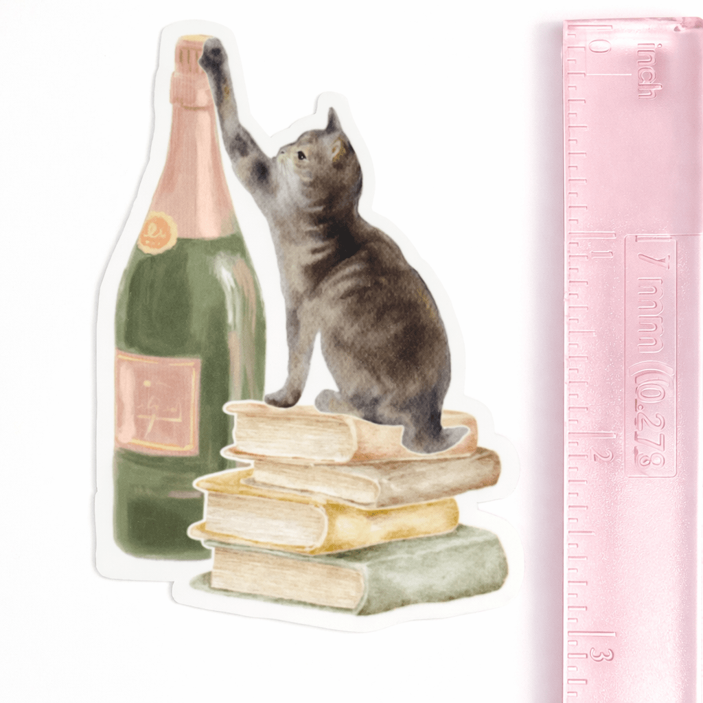 Vinyl sticker of a cat standing on books next to a bottle and a ruler for scale 