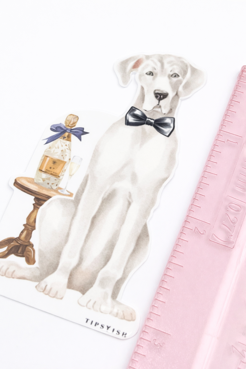 Decorative sticker with a grey dog and bottle, with a pink ruler for scale on a white background