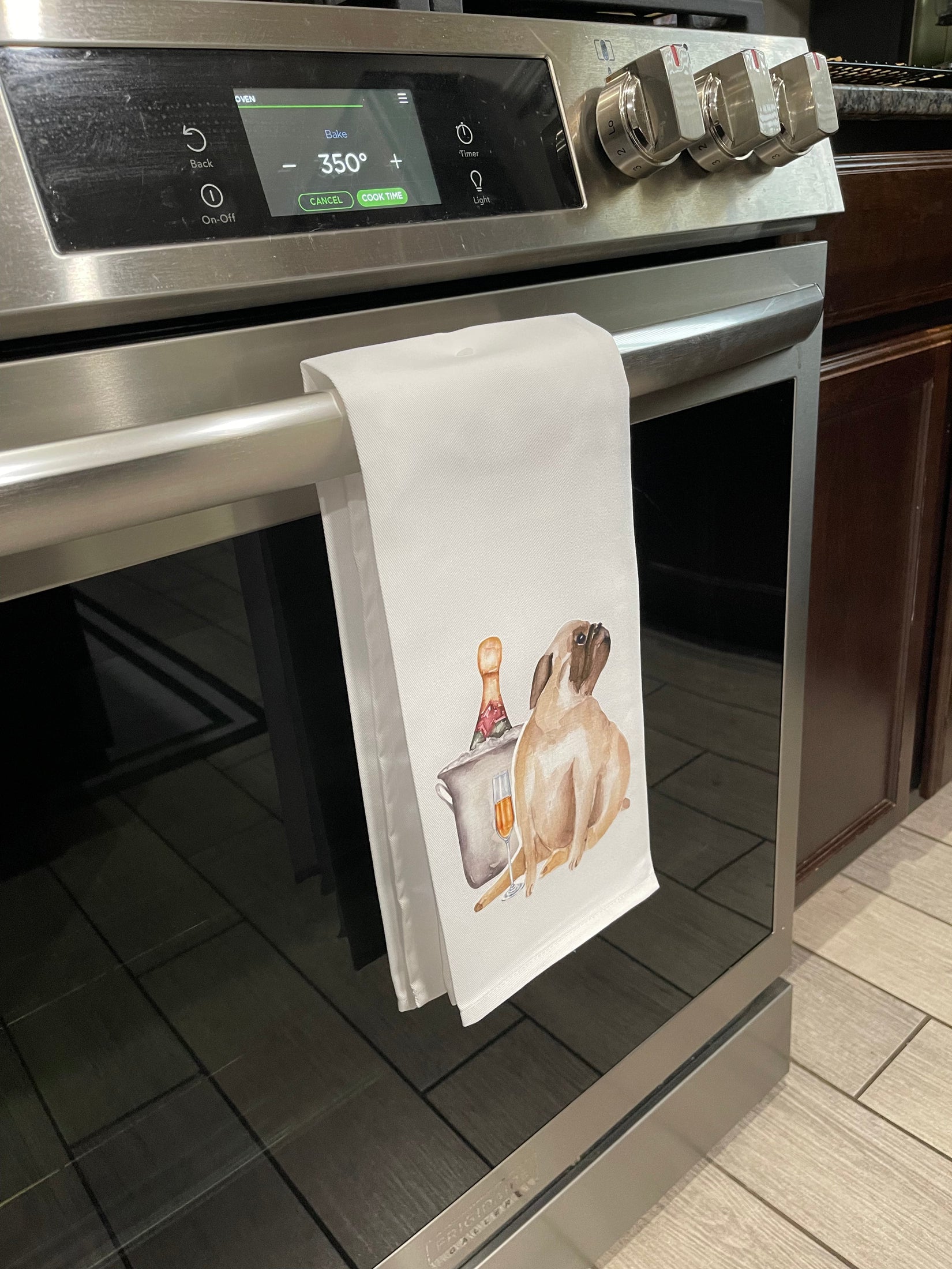 Stainless steel oven with a towel featuring a dog and bottle design hanging on the handle.