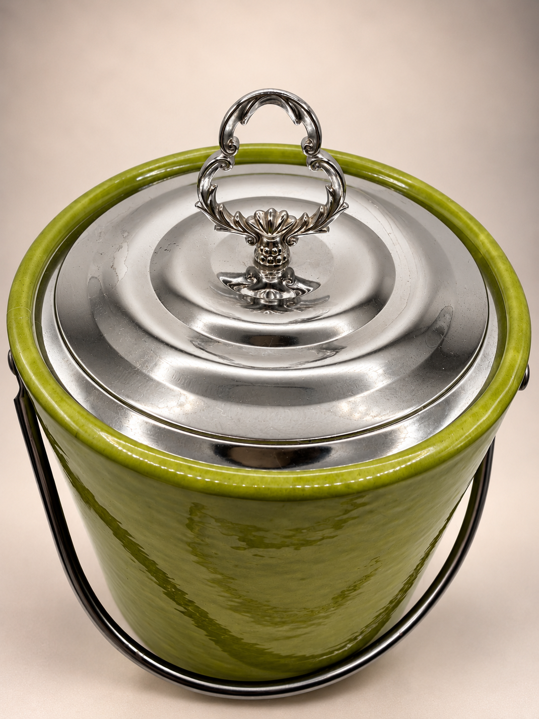Elevated view of vintage avocado-green Irvinware ice bucket showing silver-tone lid and decorative floral scrollwork handle.