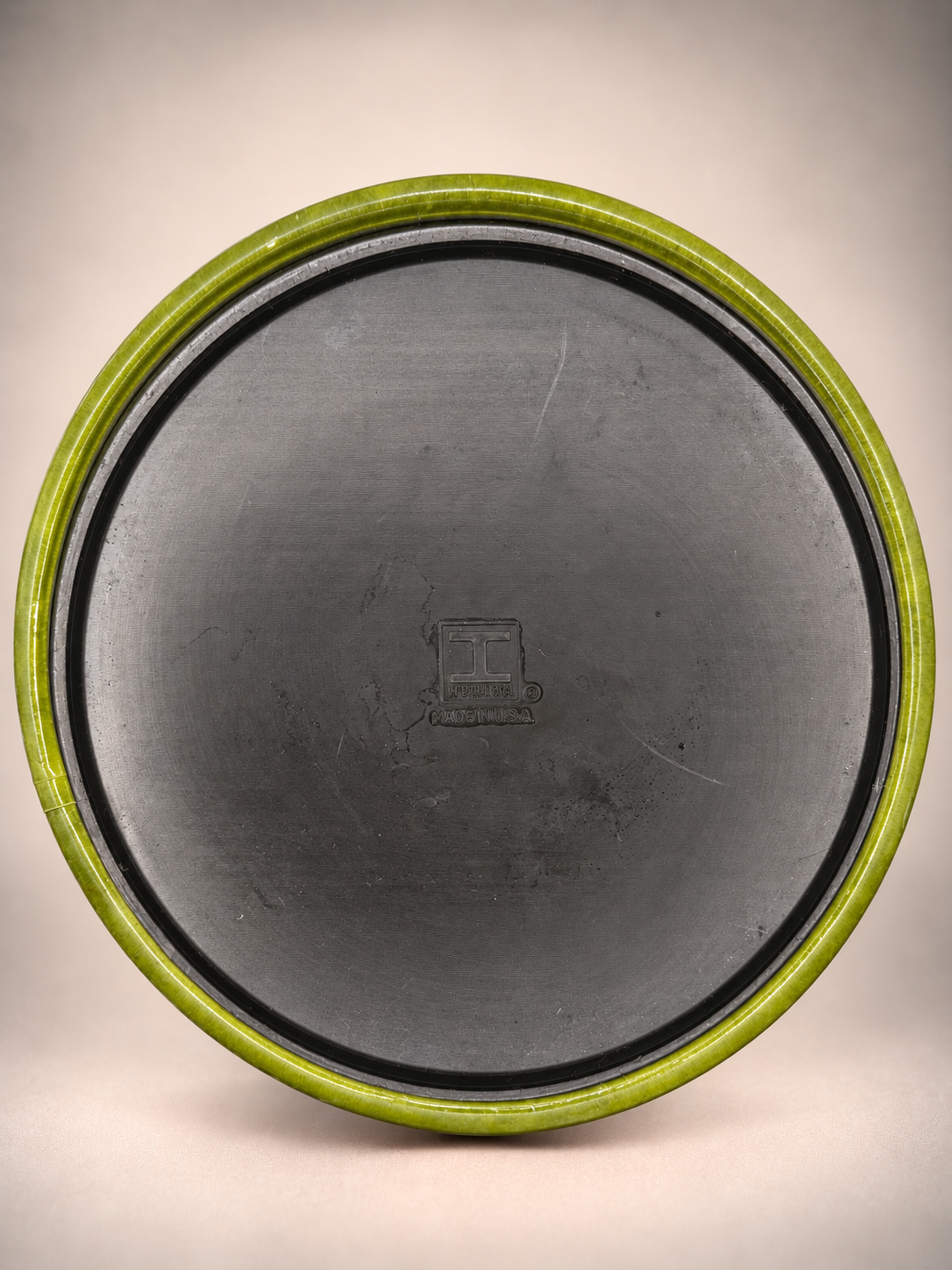 Bottom of vintage olive-green Irvinware ice bucket showing dark base, original manufacturer marking, and surface wear.
