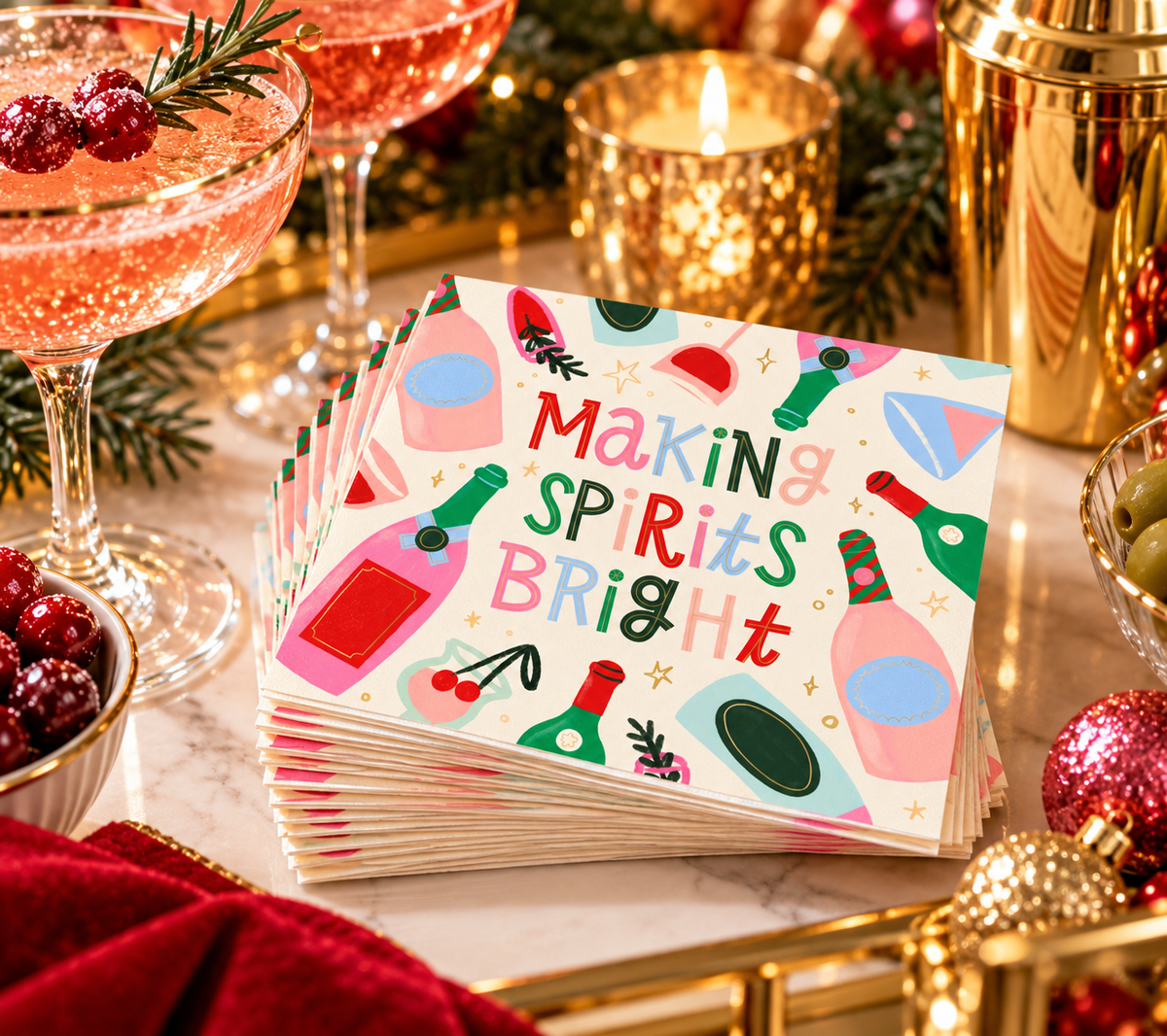Making Spirits Bright cocktail napkins styled for a festive holiday cocktail party with pink drinks, gold barware, cranberries and Christmas decorations.