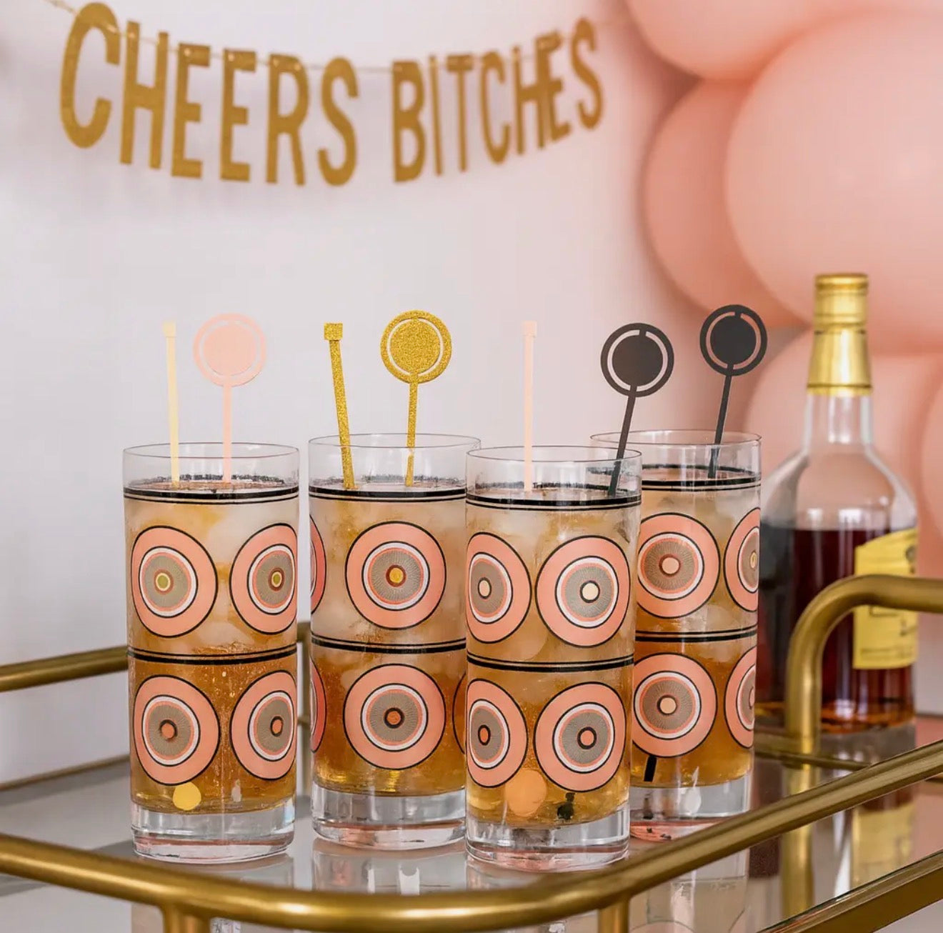 Atomic-inspired swizzle sticks styled in highball glasses on a vintage-inspired brass bar cart for entertaining.