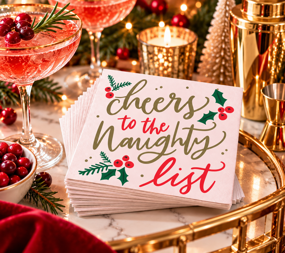 Cheers to the Naughty List Christmas cocktail napkins styled on a festive holiday bar cart with cranberry cocktails, gold barware, greenery, and Christmas lights.